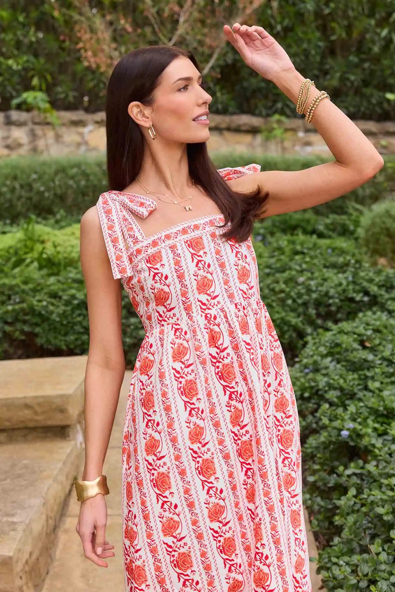 Woman wearing a red and white patterned dress standing outdoors with greenery in the background