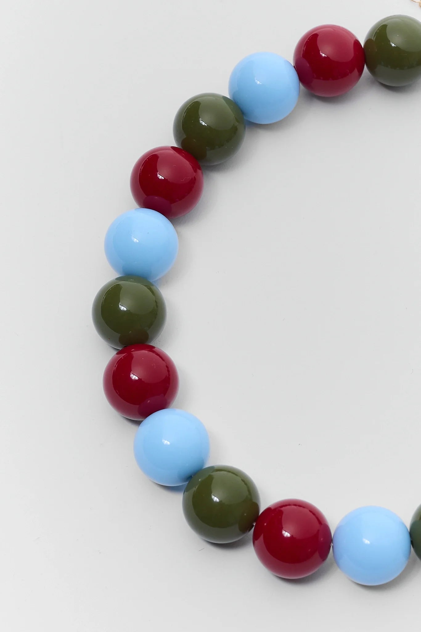 A beaded stretch bracelet featuring glossy, round beads in red, light blue, olive green, and dark green, arranged in a curved shape on a light gray background.