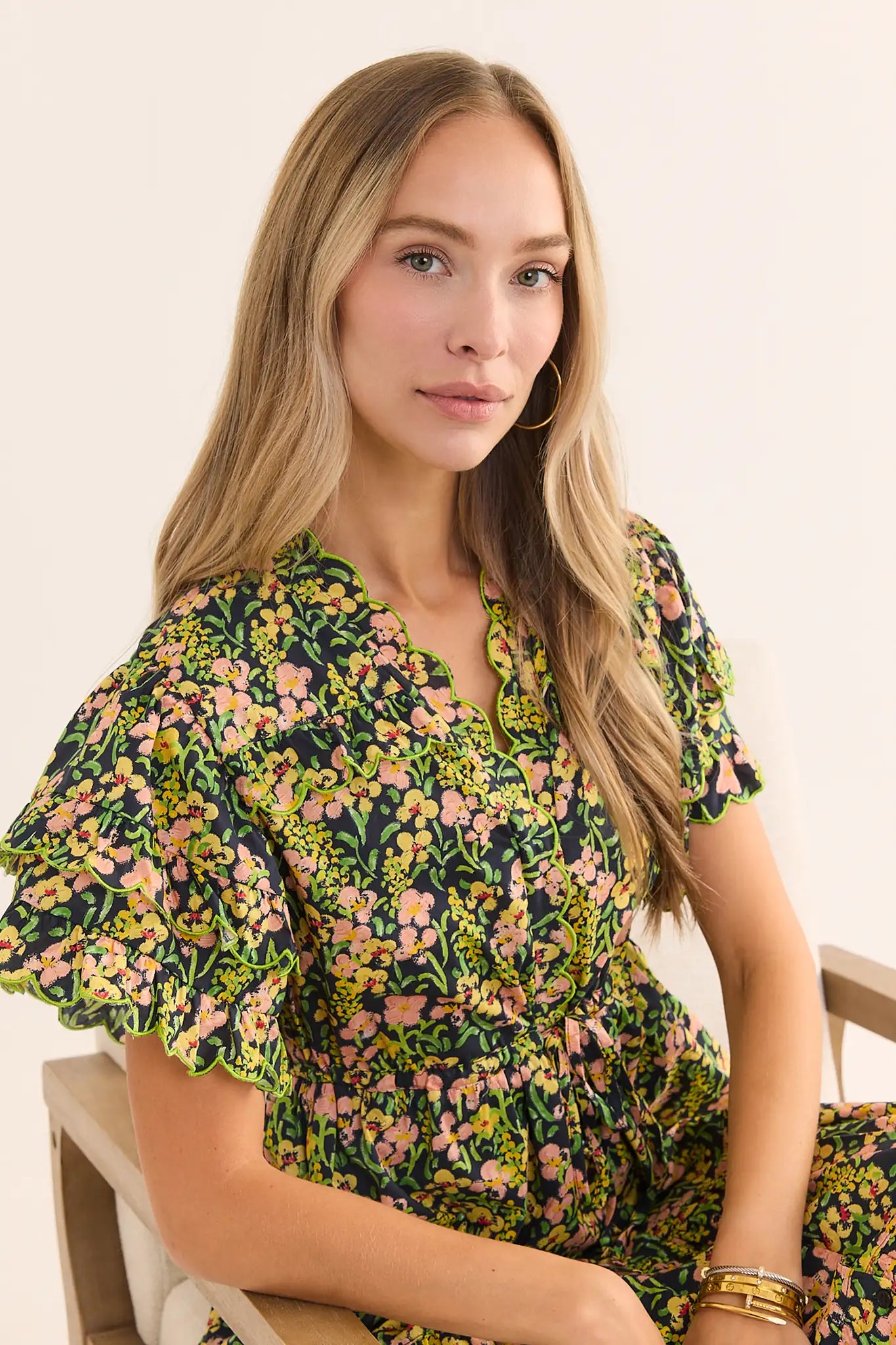 close up A woman modeling a long-sleeved, V-neck maxi dress with a green, yellow, and pink floral print, against a plain light beige studio background.