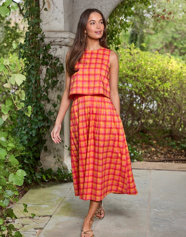 Woman wearing a red and yellow checkered dress standing in a garden setting.