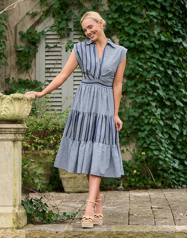 Woman in a blue striped dress standing outdoors with greenery in the background
