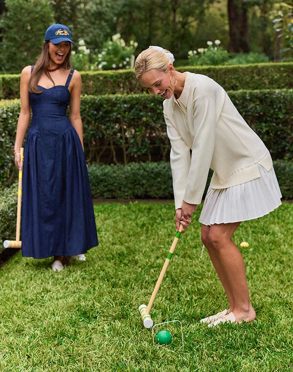Two women playing croquet on a grassy lawn with hedges in the background.