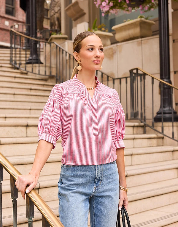 Woman in a pink striped shirt and blue jeans standing on outdoor steps. navigation
