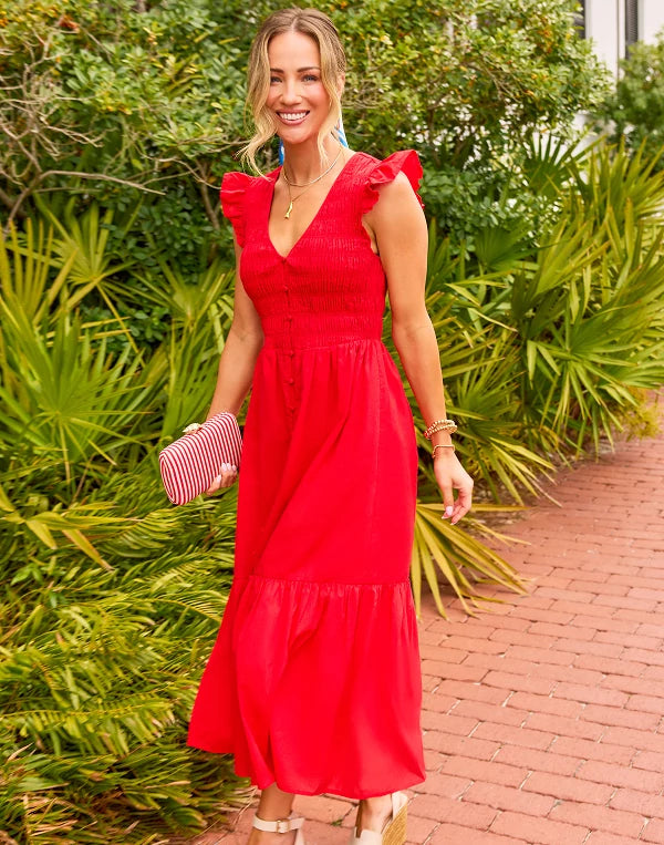 Woman in a red dress standing outdoors with greenery in the background nav