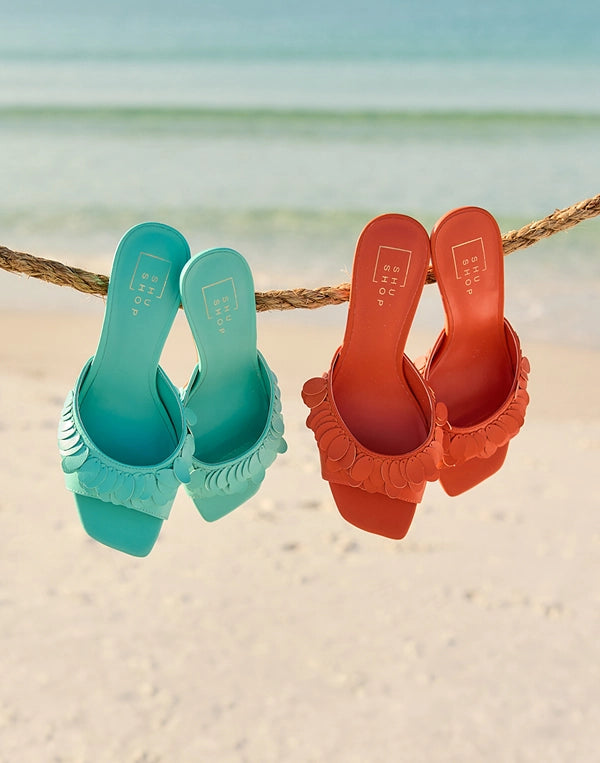 Turquoise and orange sandals hanging on a rope with a beach background nav