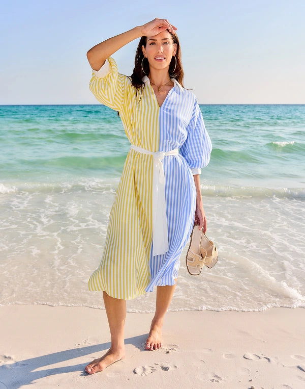 Woman in a colorful striped dress standing on a beach with ocean in the background nav