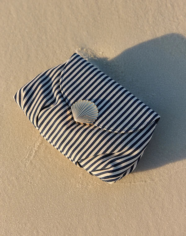 Striped pouch with a shell on a sandy surface nav