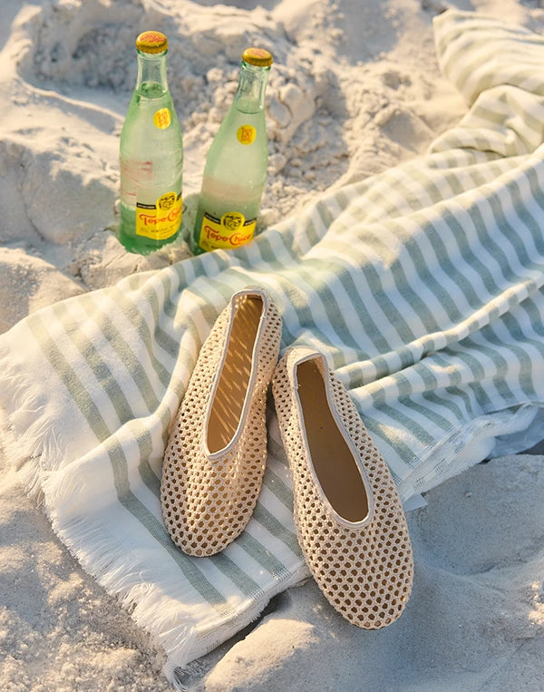 Pair of beige perforated shoes on a sandy surface with two bottles of Perrier in the background nav