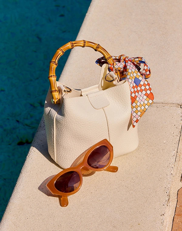 White handbag with bamboo handle and sunglasses on a ledge by a body of water navigation