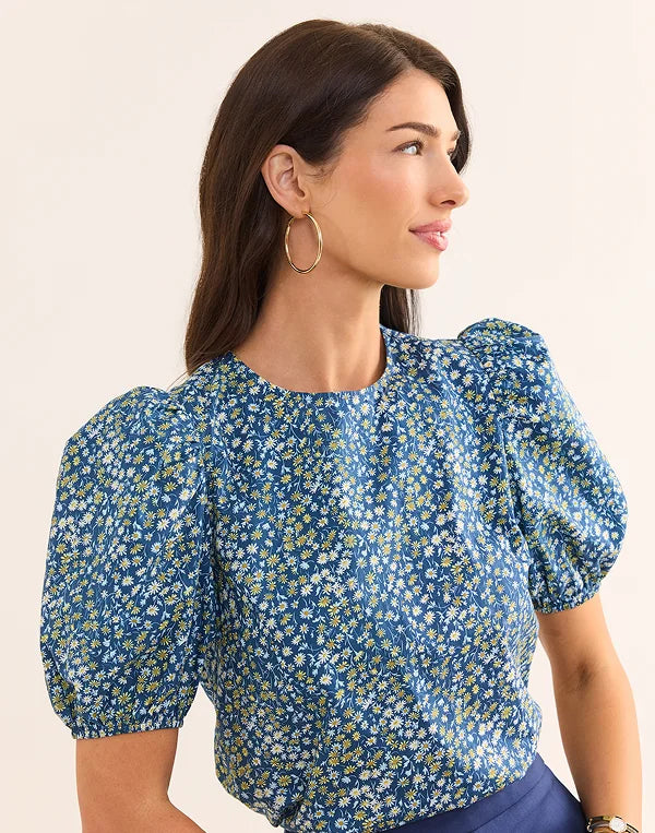 Woman wearing a blue floral blouse with puffed sleeves on a beige background nav