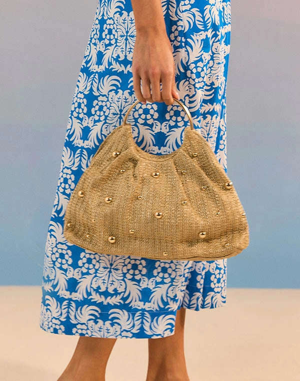 Person holding a straw handbag with a blue and white patterned dress in the background