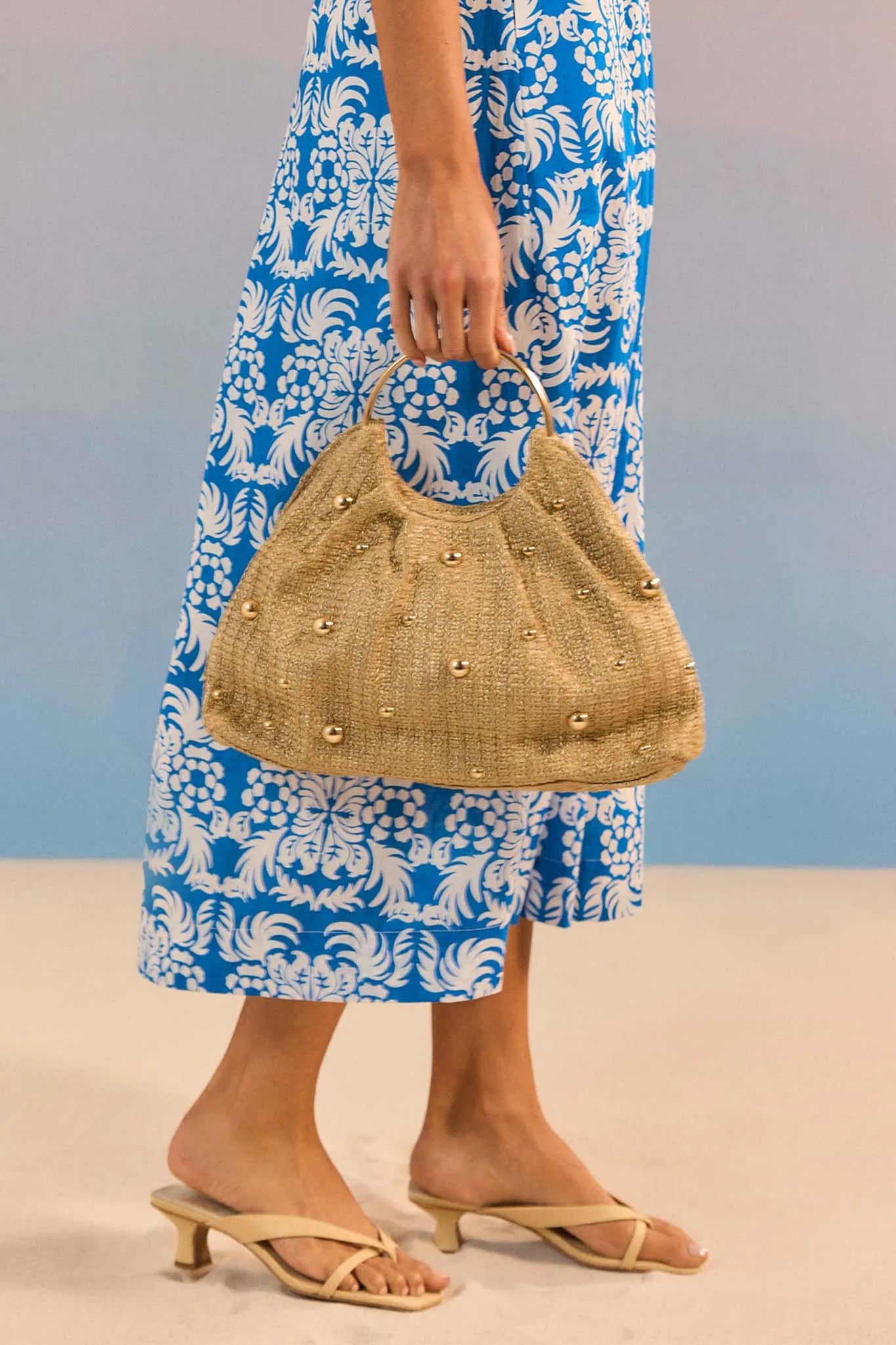 Person holding a straw handbag wearing a blue and white patterned dress.