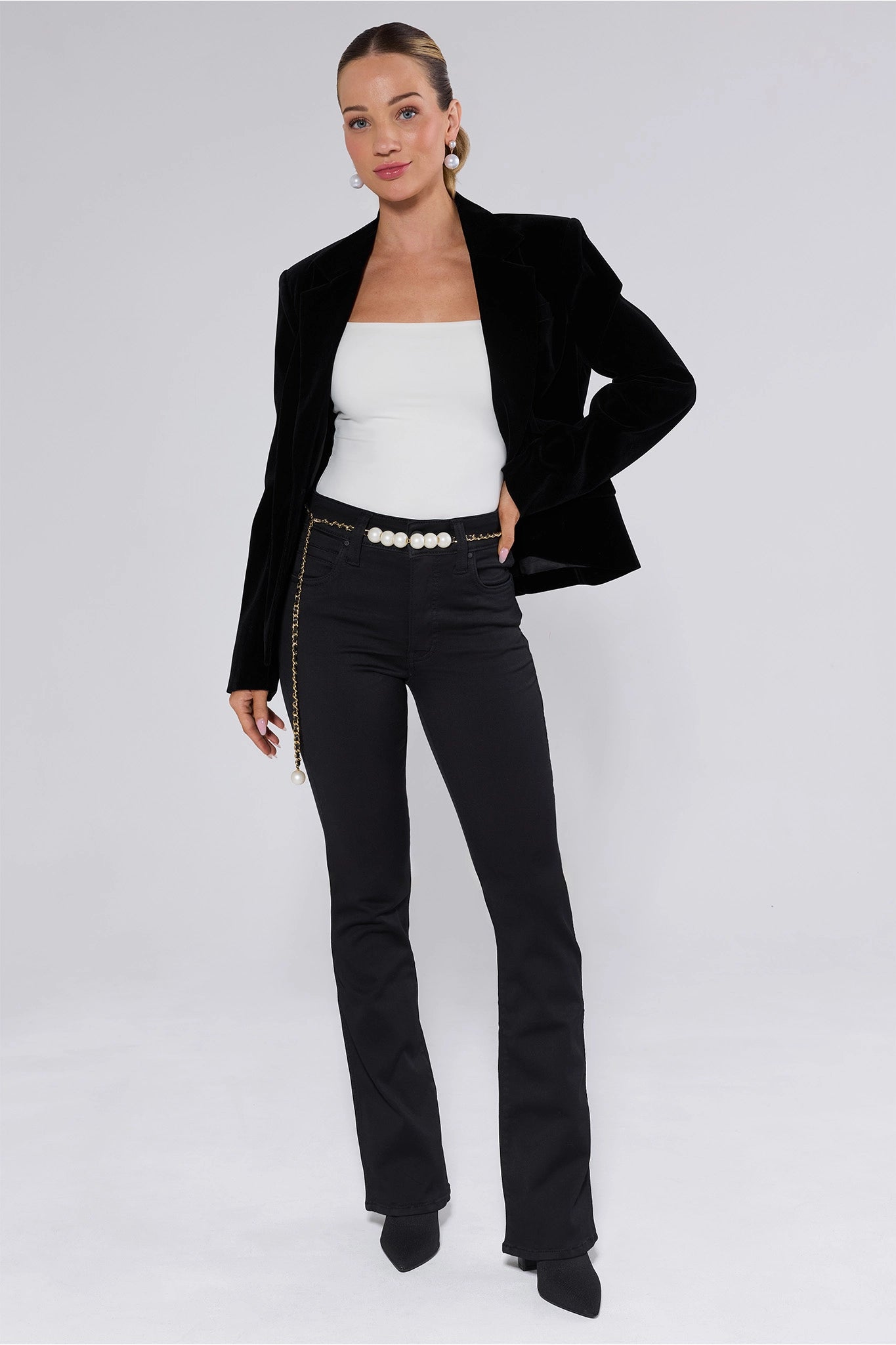 Woman wearing a black blazer, white top, and black Natalie Jeans on a white background