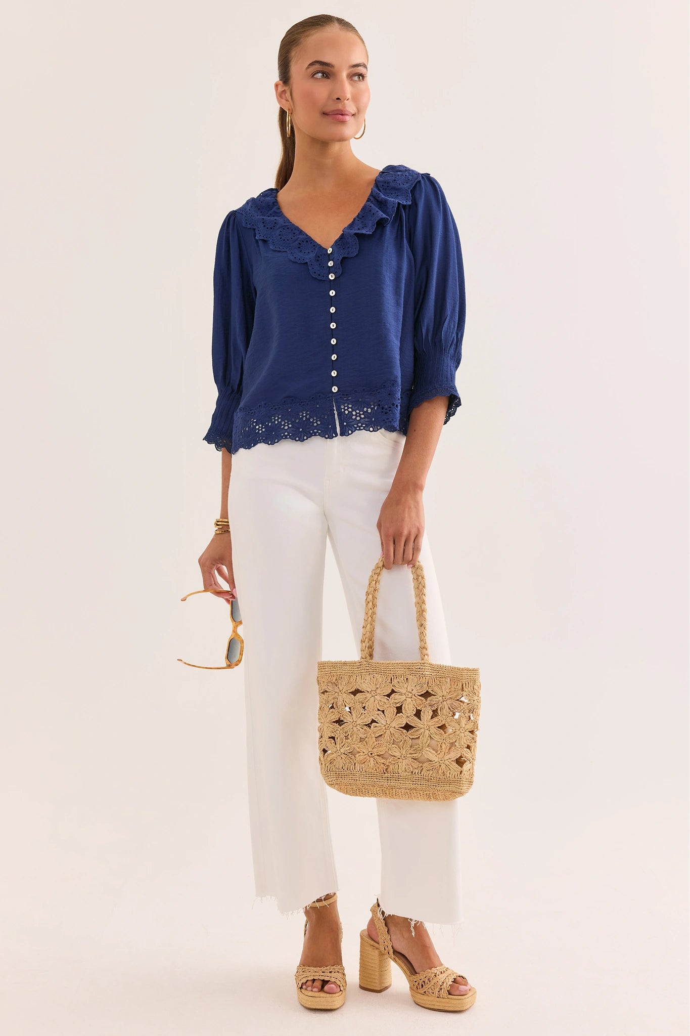 Woman wearing a blue blouse and white pants, holding a straw bag on a white background