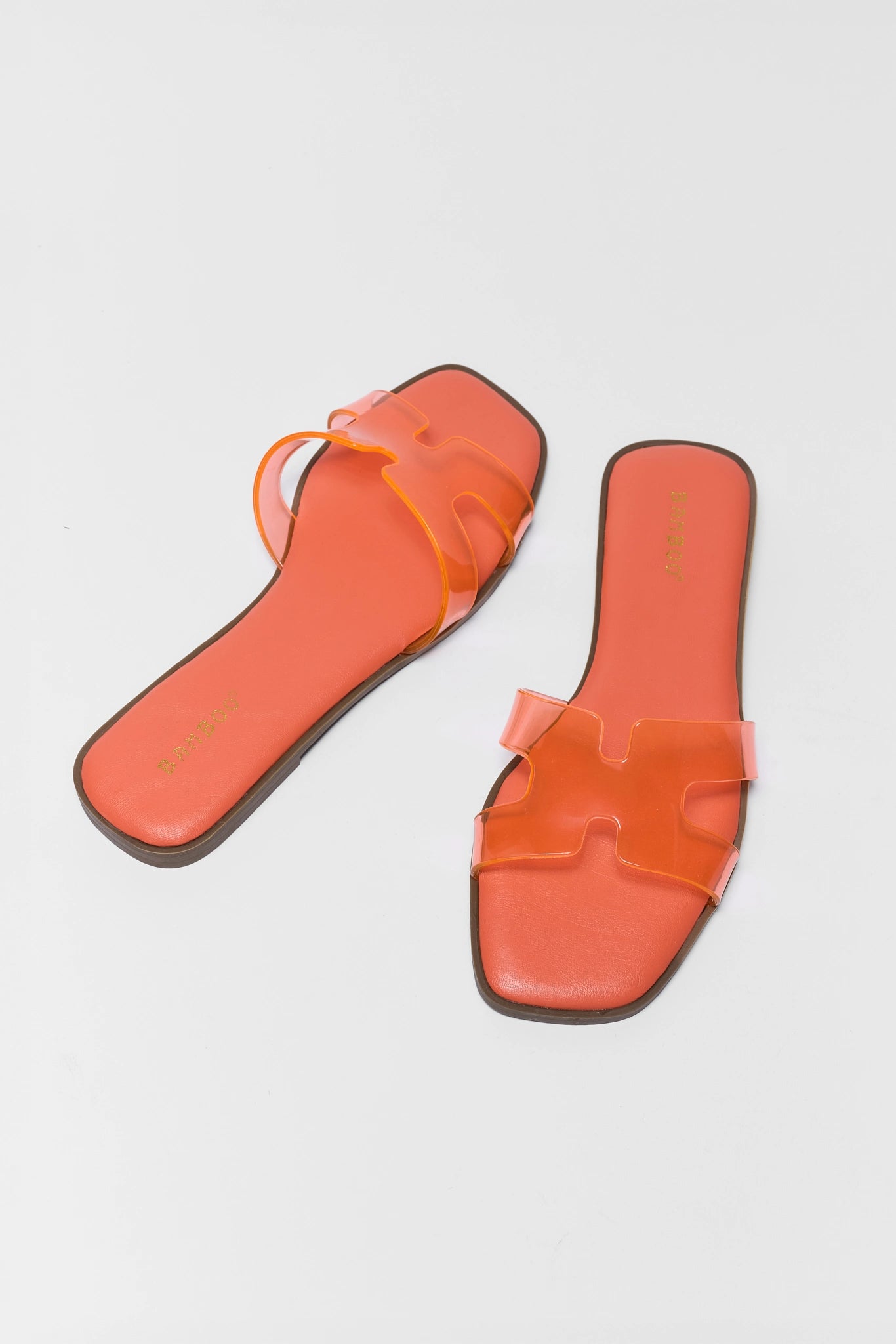 Orange sandals with clear straps on a light gray background