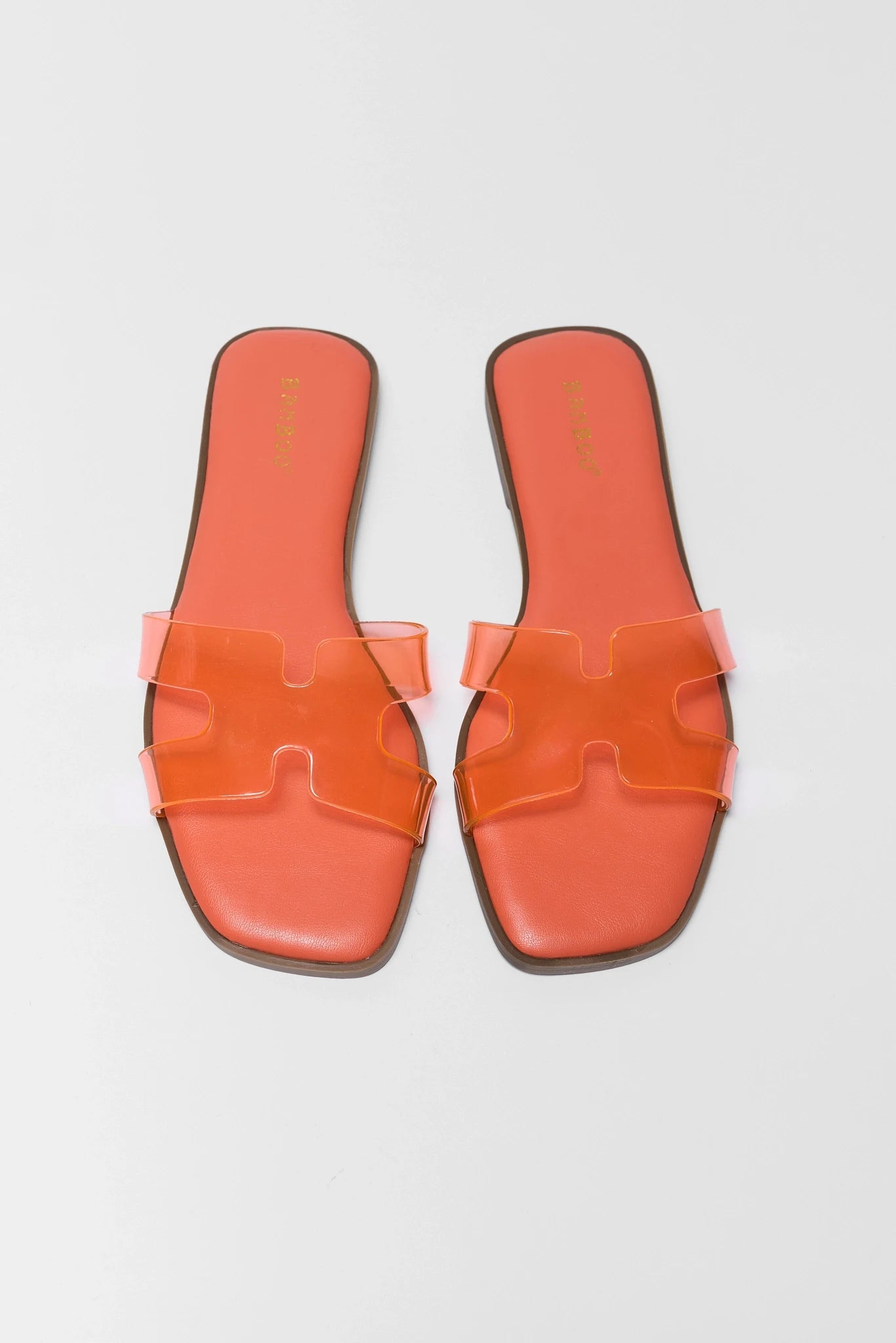 Pair of orange sandals with a distinctive buckle design on a gray background