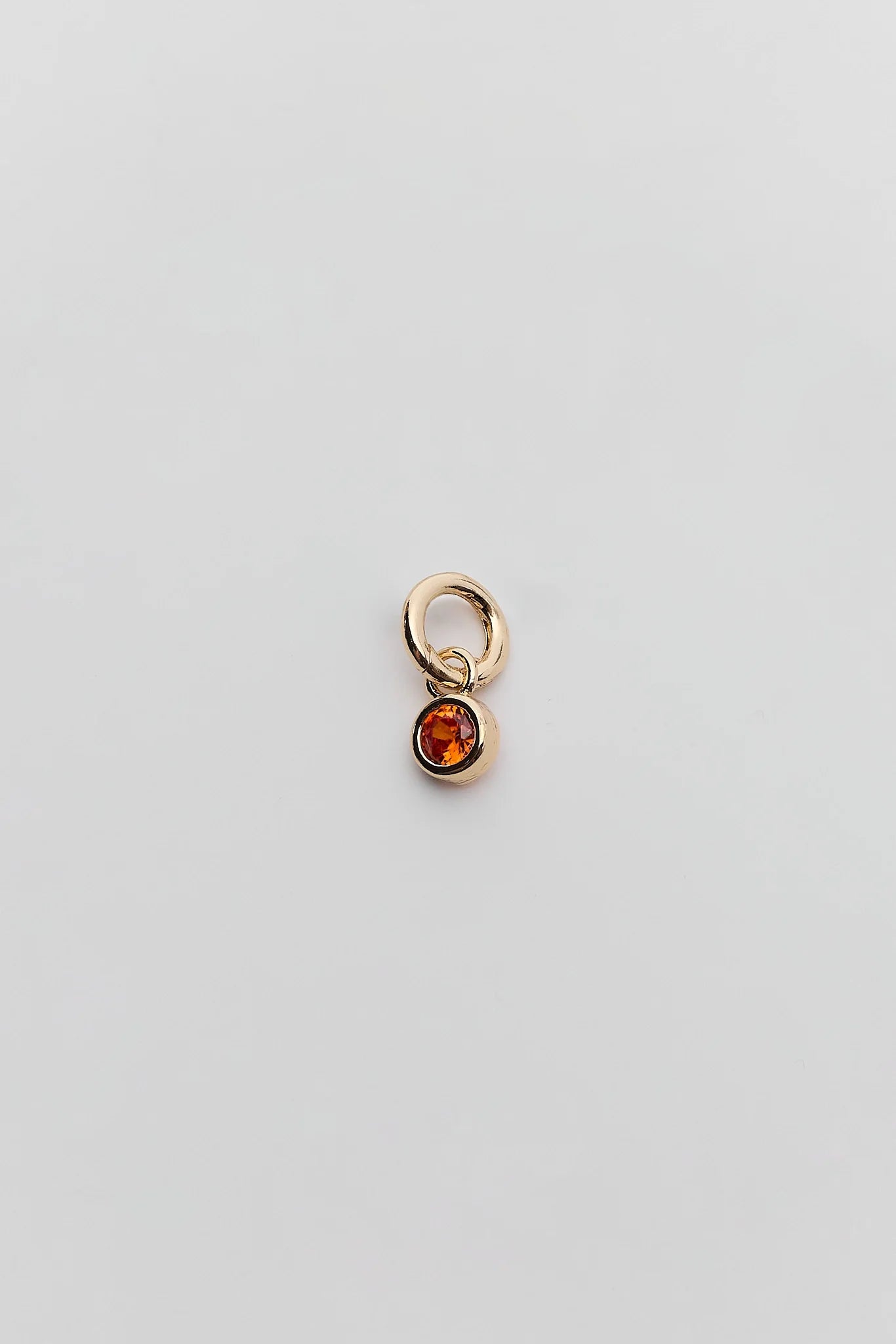 A small gold charm featuring a dangling oval amber gemstone, centered on a plain light gray background.