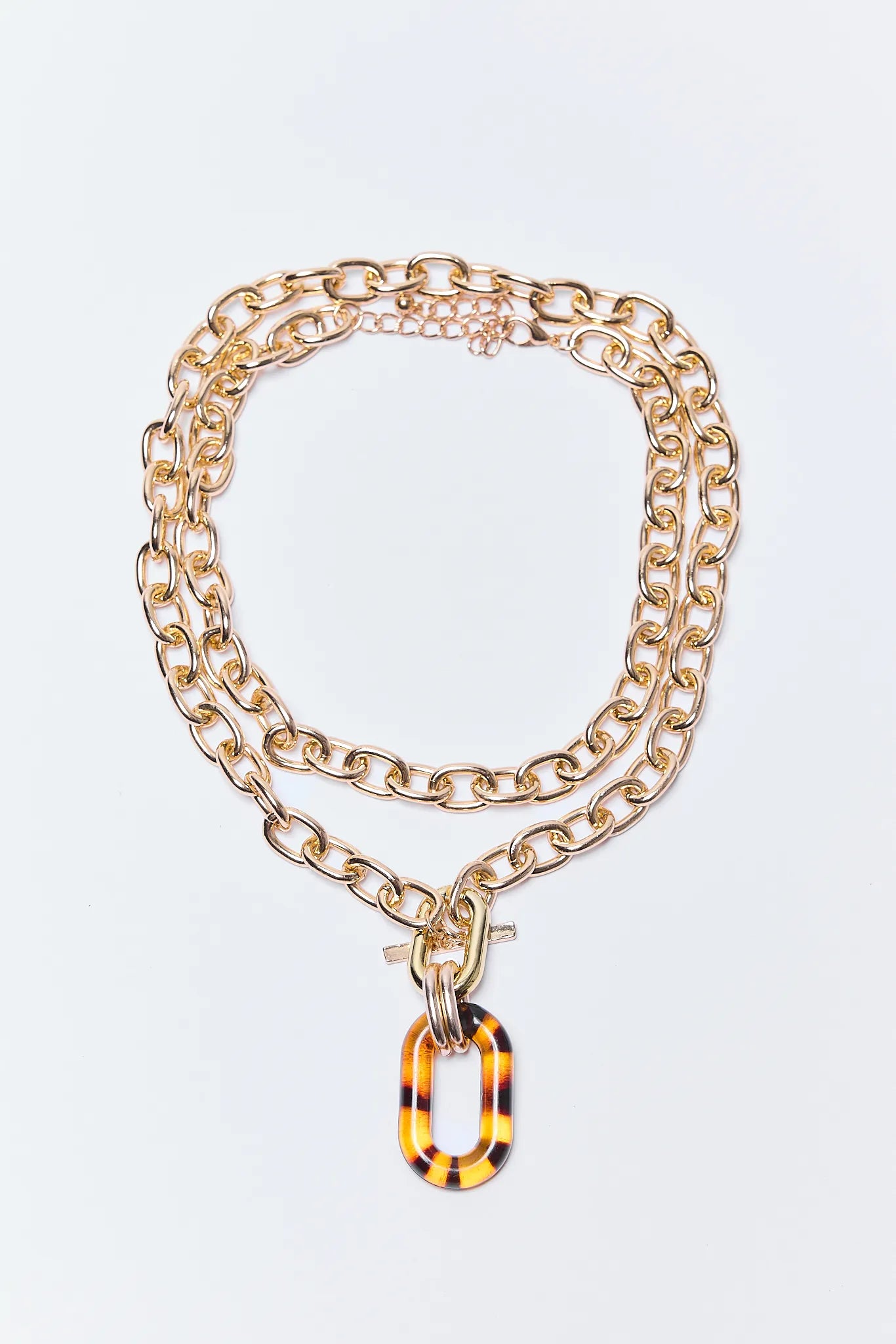 Gold chain Pippa Necklace with a tortoiseshell pendant on a light gray background