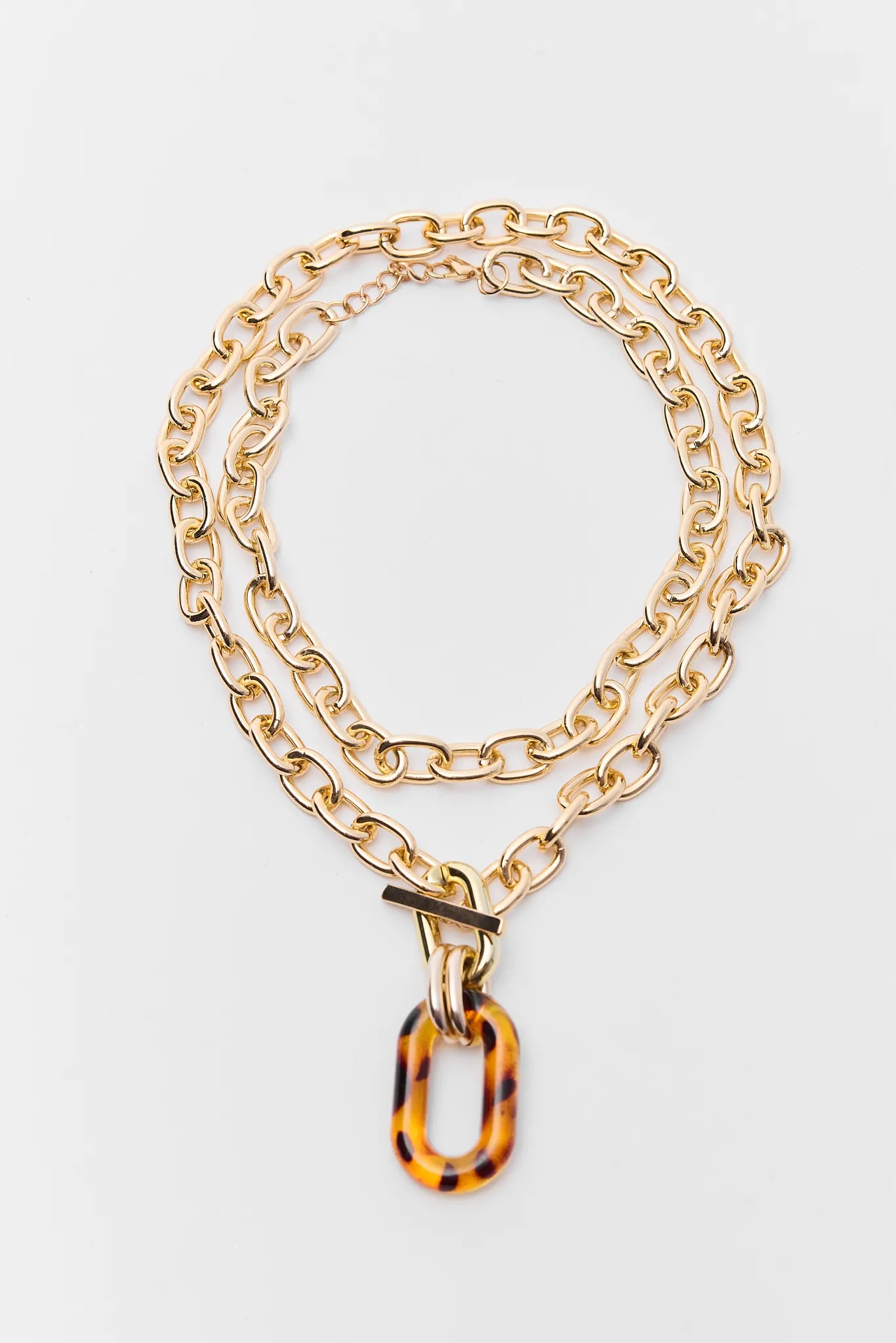 Gold chain necklace with a tortoiseshell pendant on a light gray background
