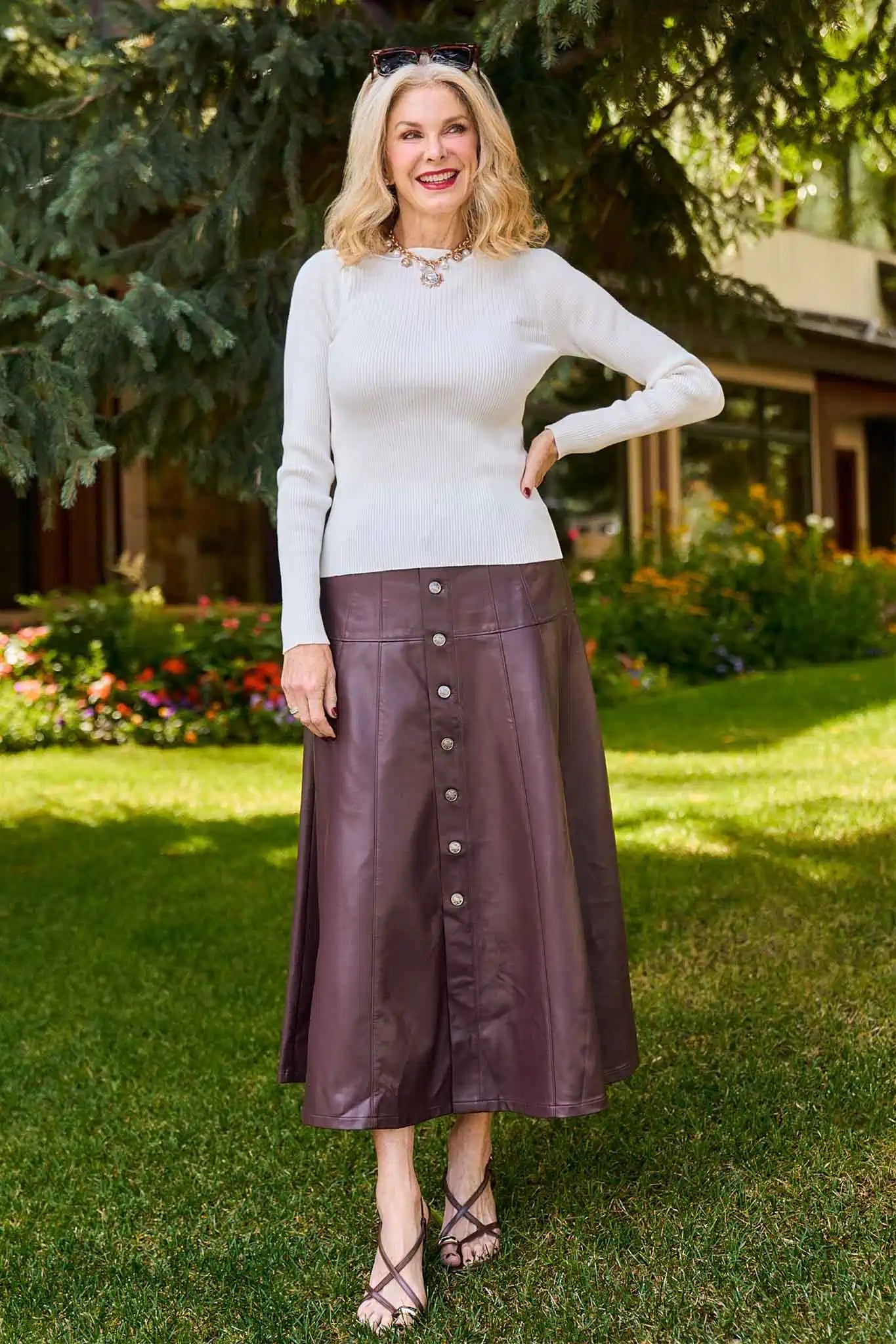 Woman wearing a white sweater and brown leather Preston Skirt standing outdoors.