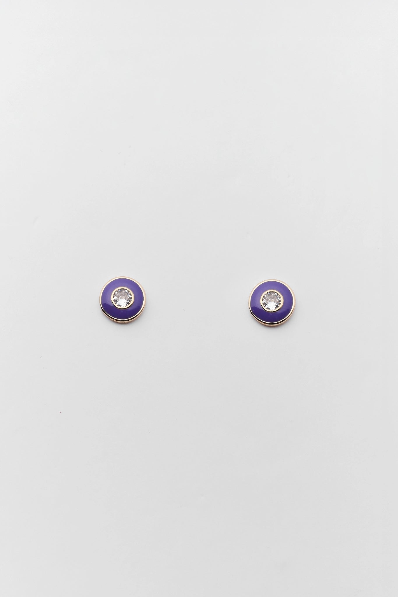 A pair of small round stud earrings with a vibrant purple enamel face, a silver-tone bezel, and a clear crystal center, displayed on a light gray background.