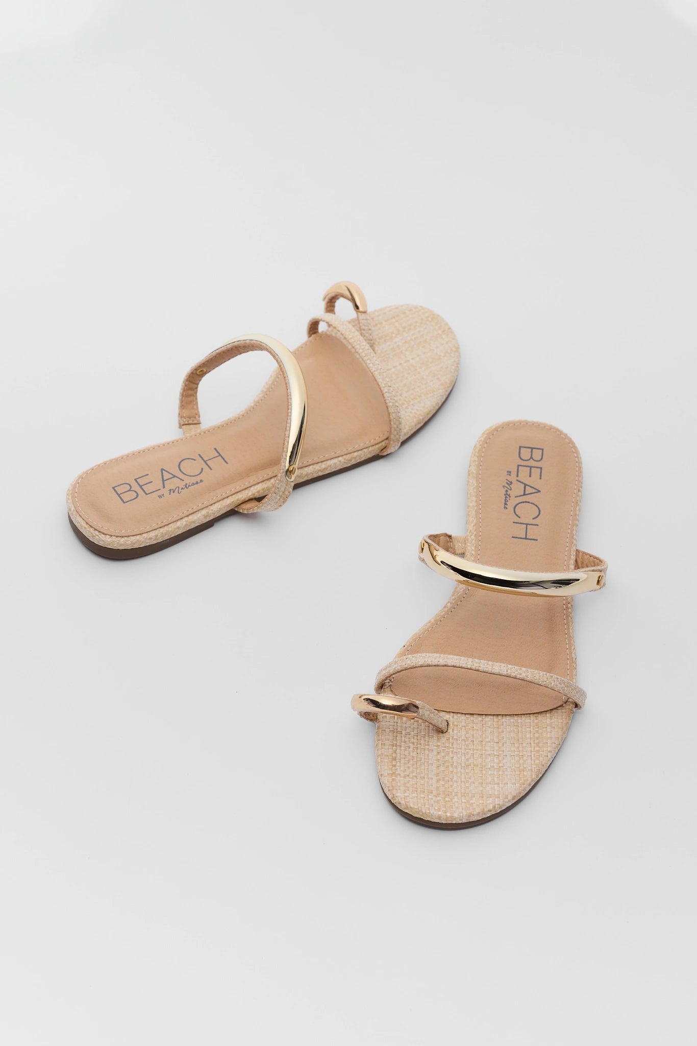 Pair of beige sandals with gold straps on a light gray background