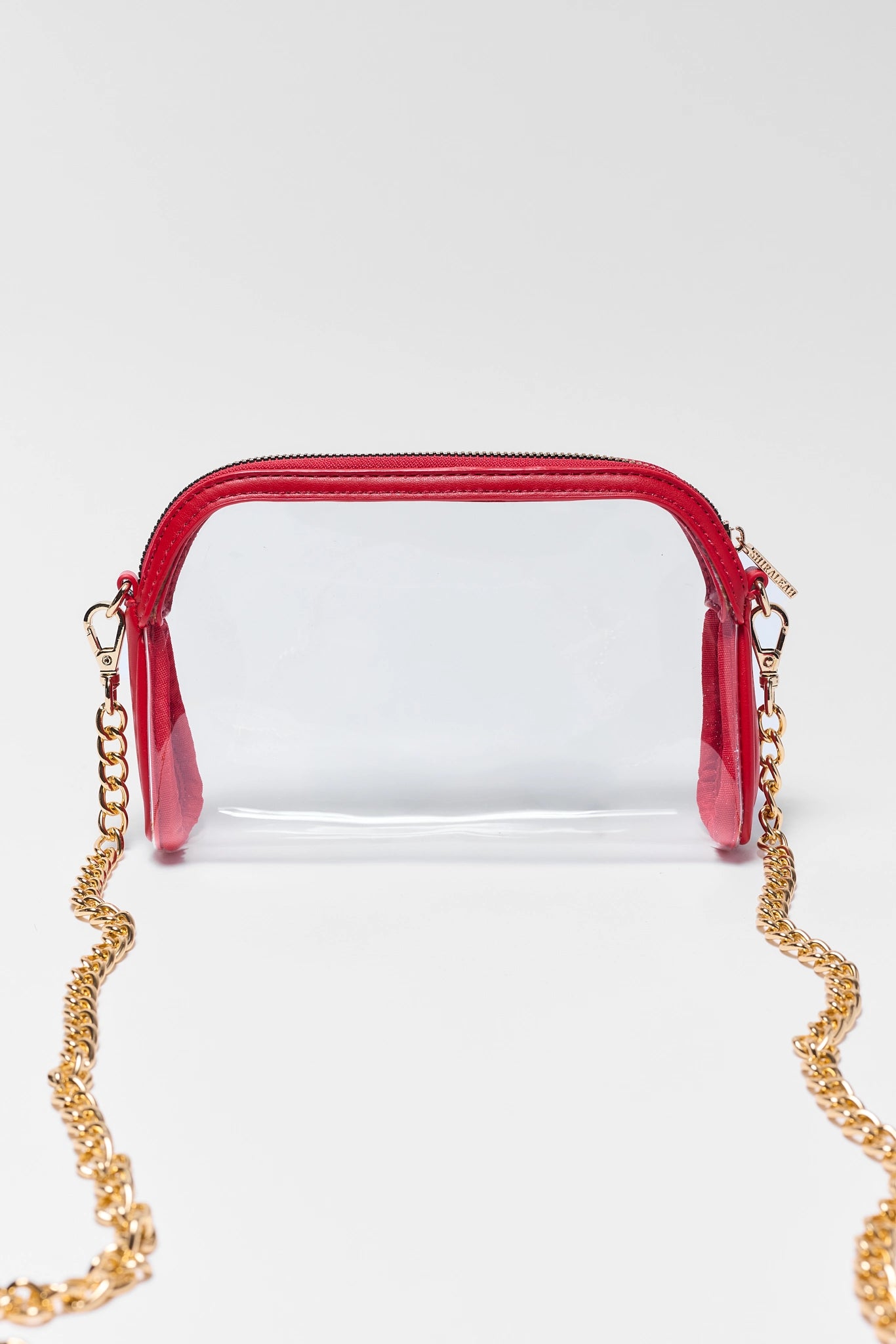 A clear plastic cosmetic pouch with a bright red zipper and trim, featuring a gold-tone chain strap, set against a plain light gray background.