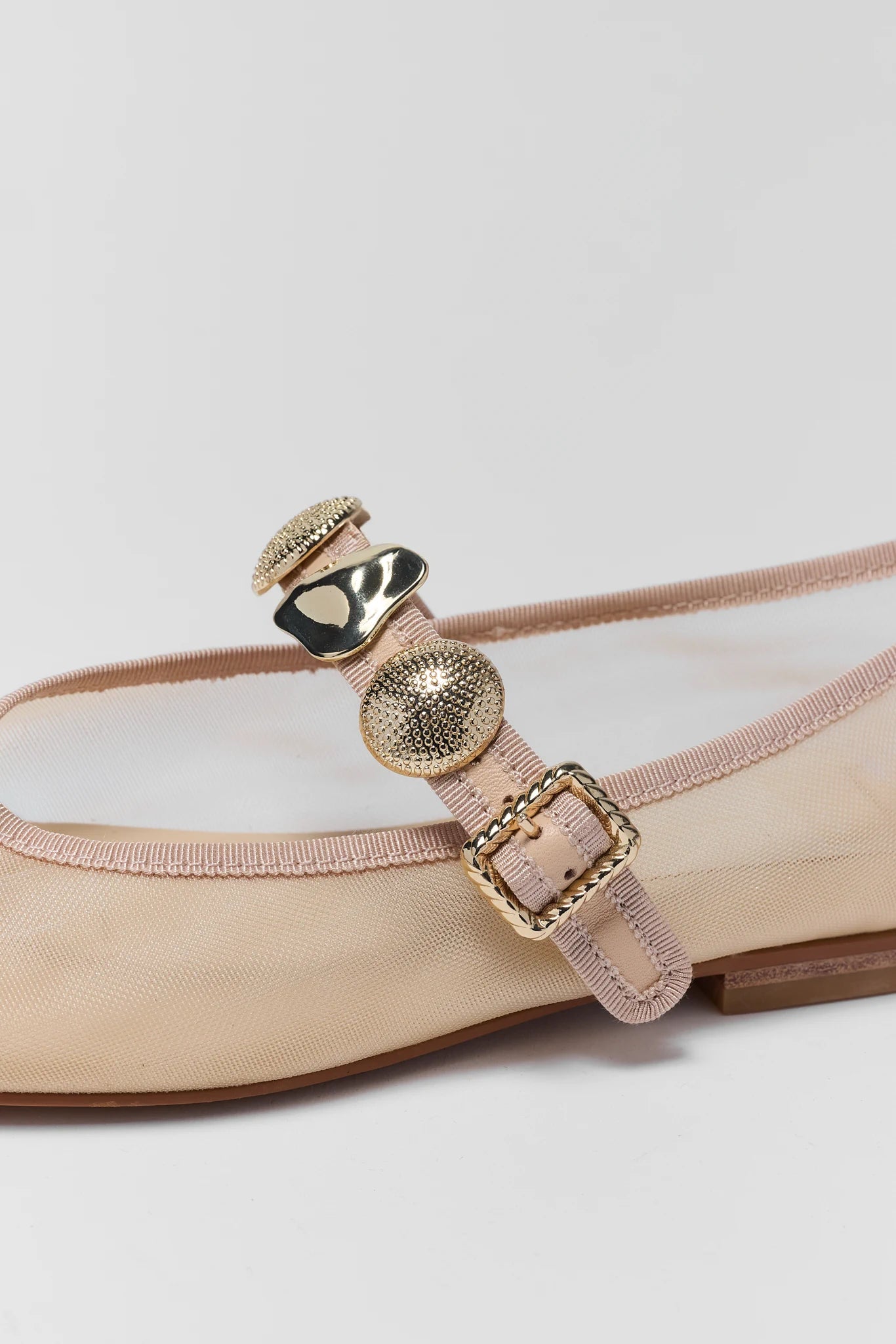 Beige flat shoe with decorative strap featuring gold elements on a white background