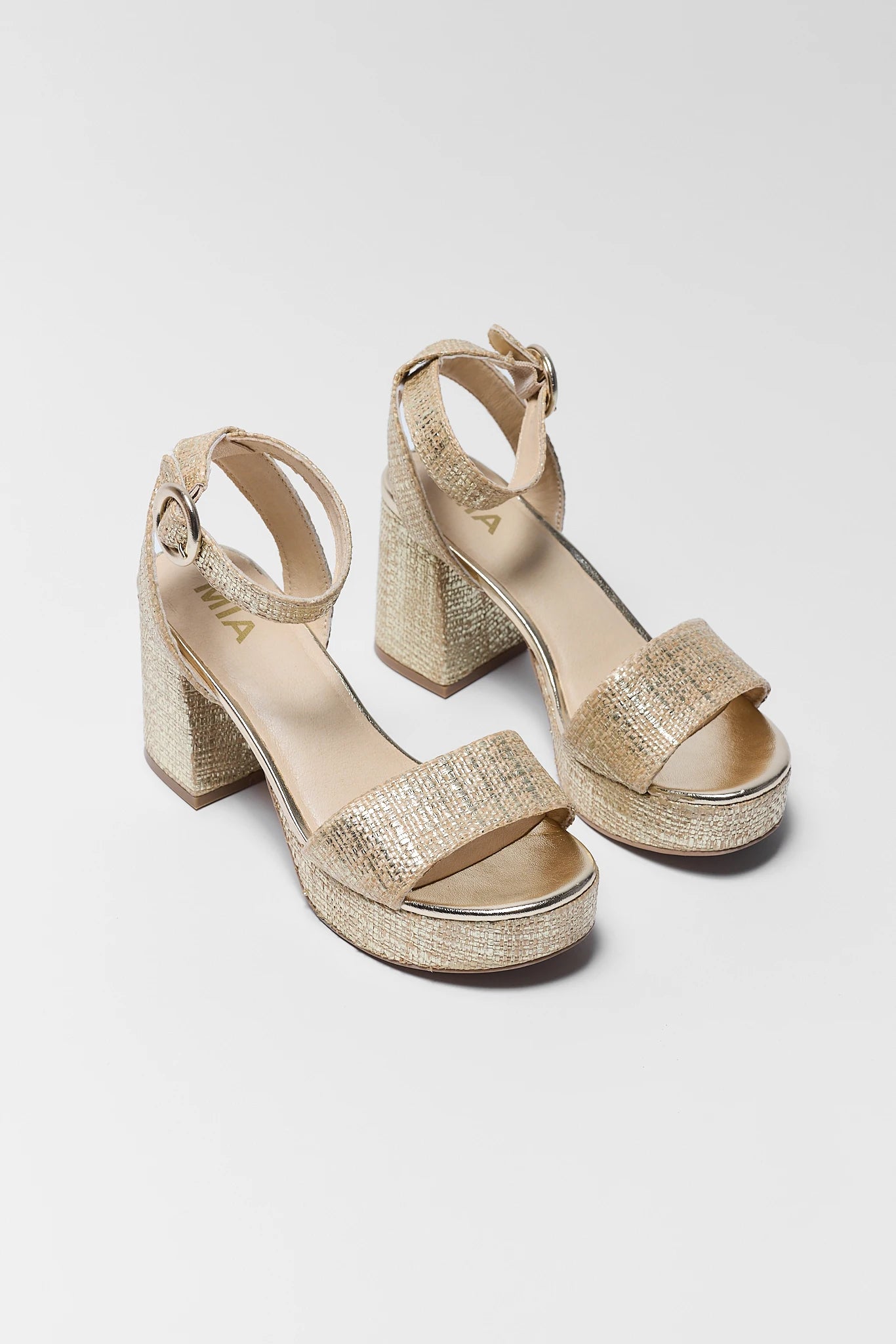 two Pair of gold glittery high-heeled sandals on a light gray background