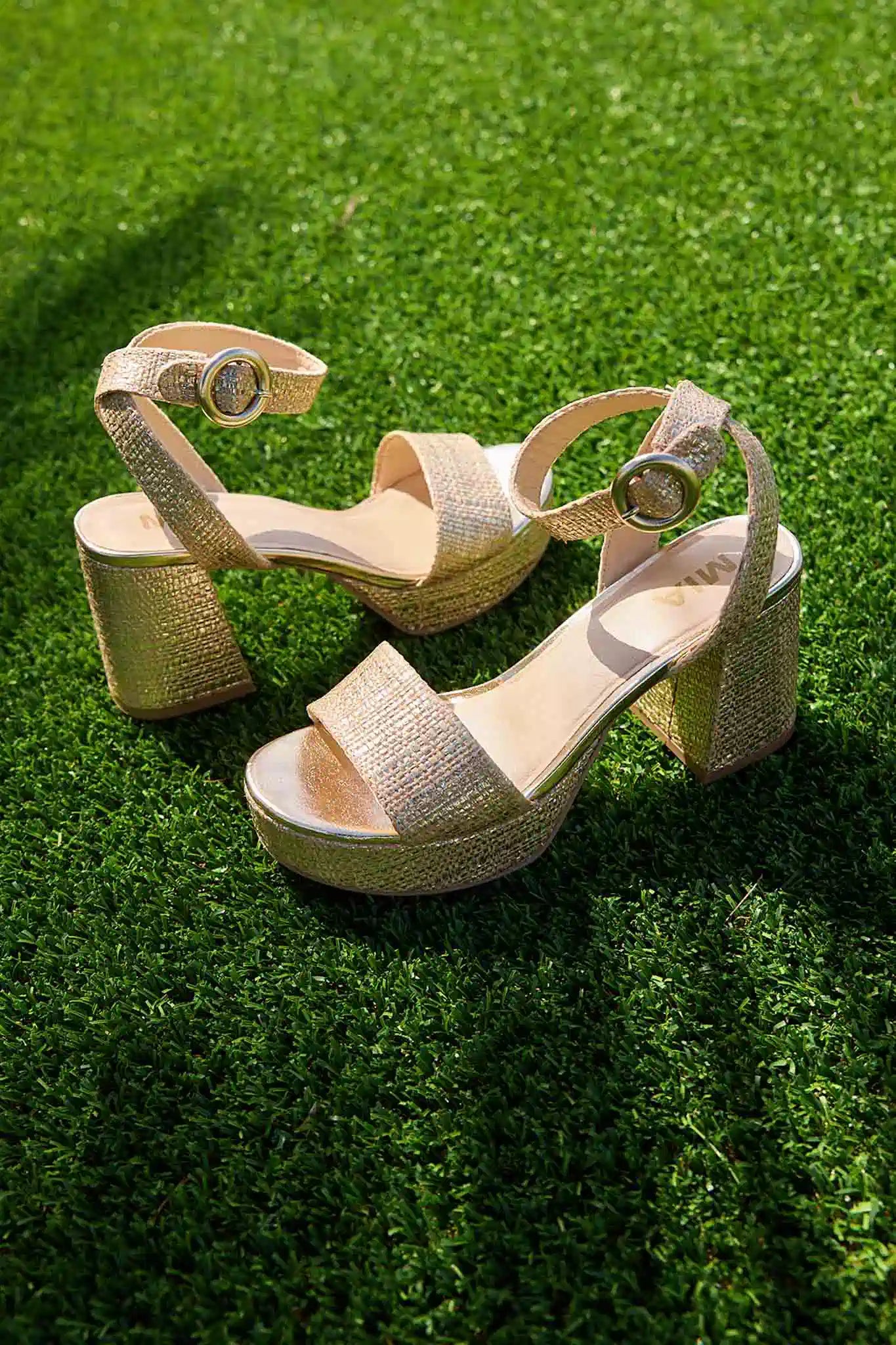 Gold glittery high-heeled sandals on a grassy background