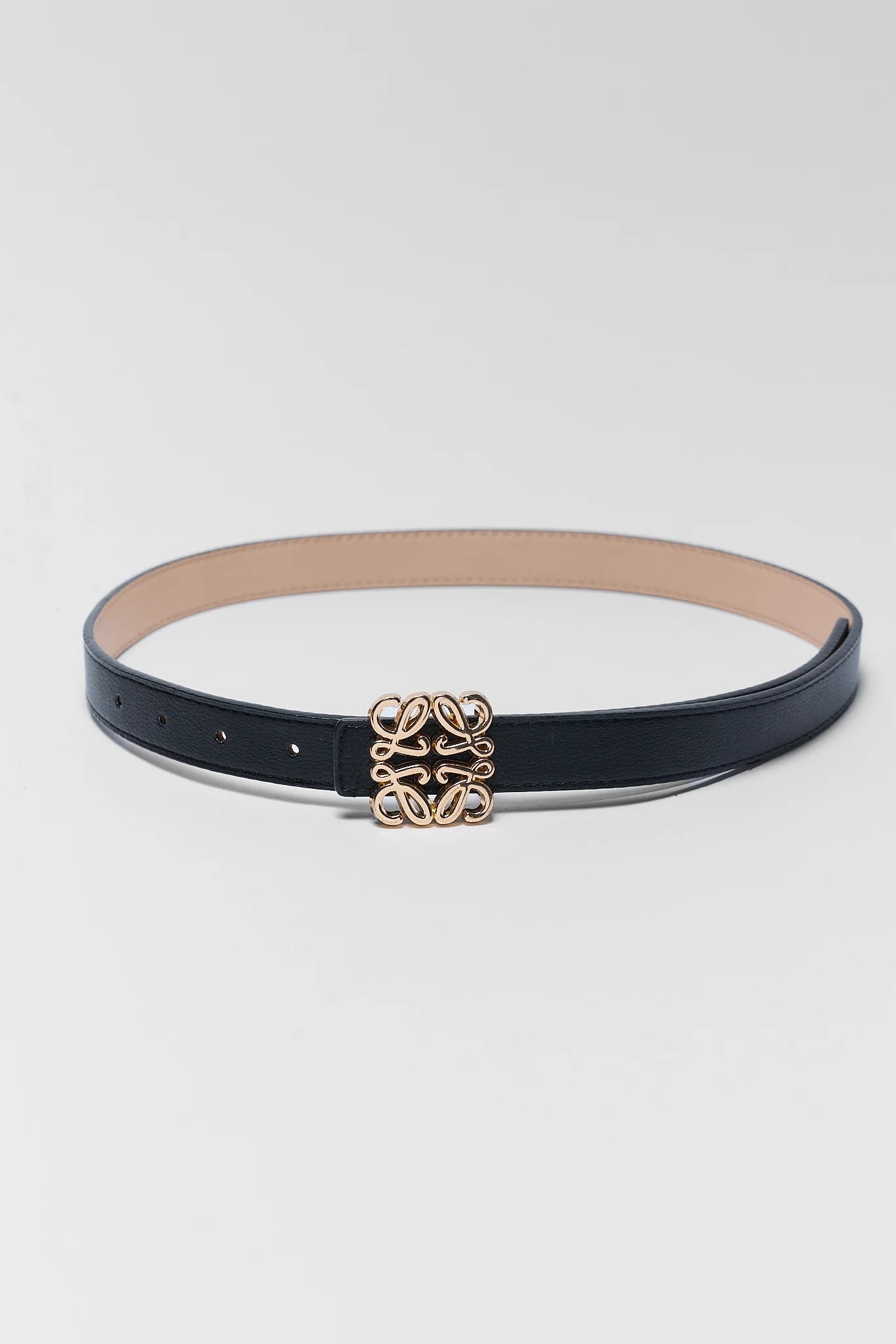 A slim black leather belt with a gold-tone interlocking logo buckle, displayed on a light gray background.
