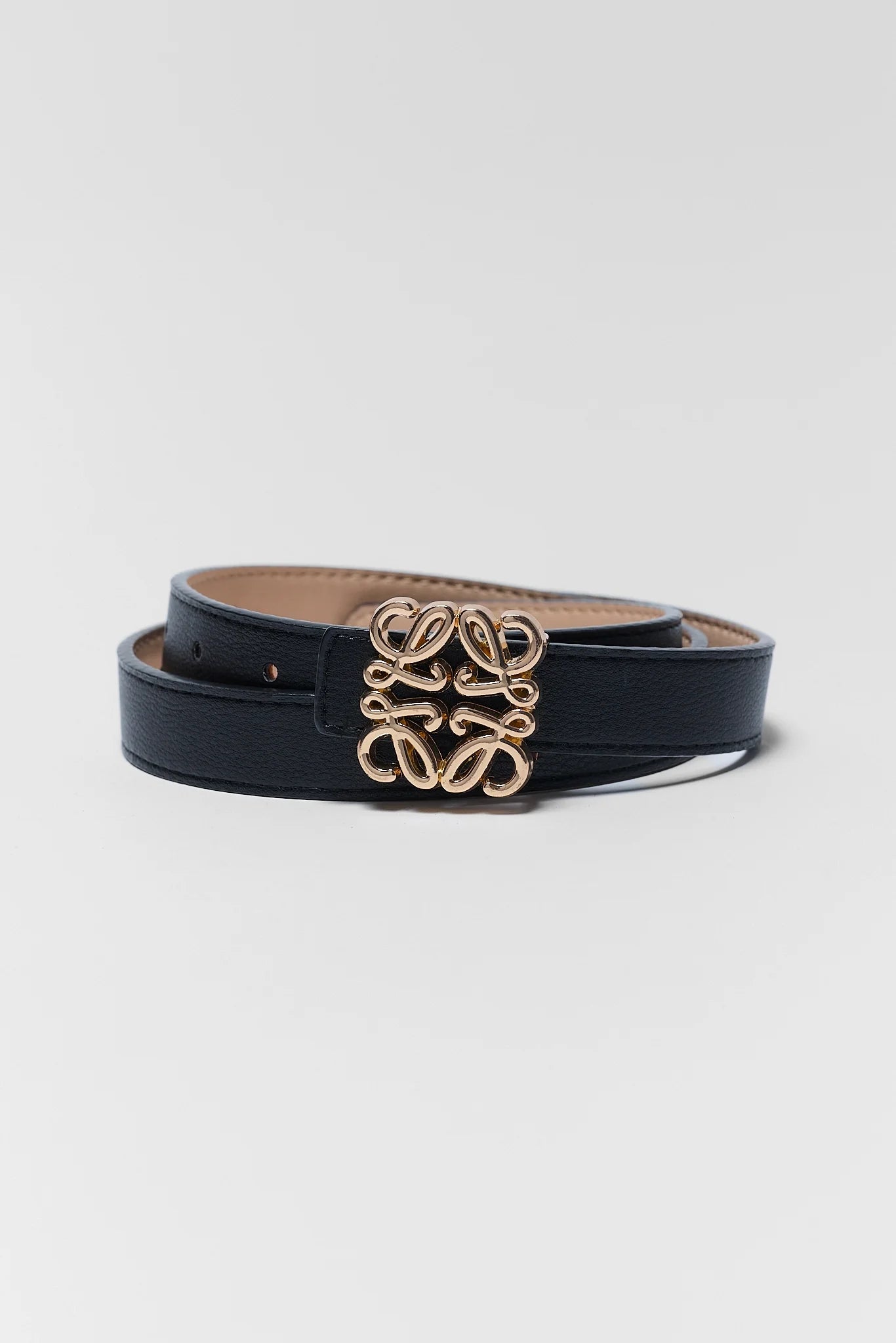 A black leather belt with a gold-tone interlocking logo buckle, coiled on a light gray background.
