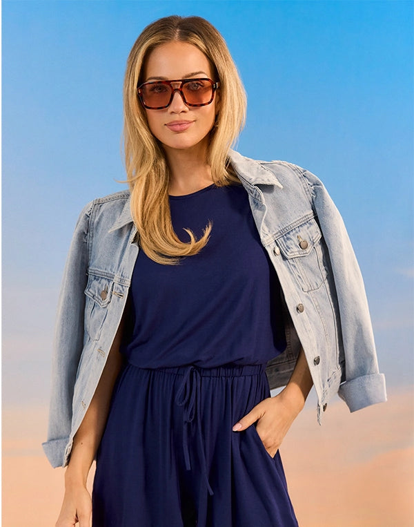 Woman wearing a denim jacket and navy dress against a blue sky.