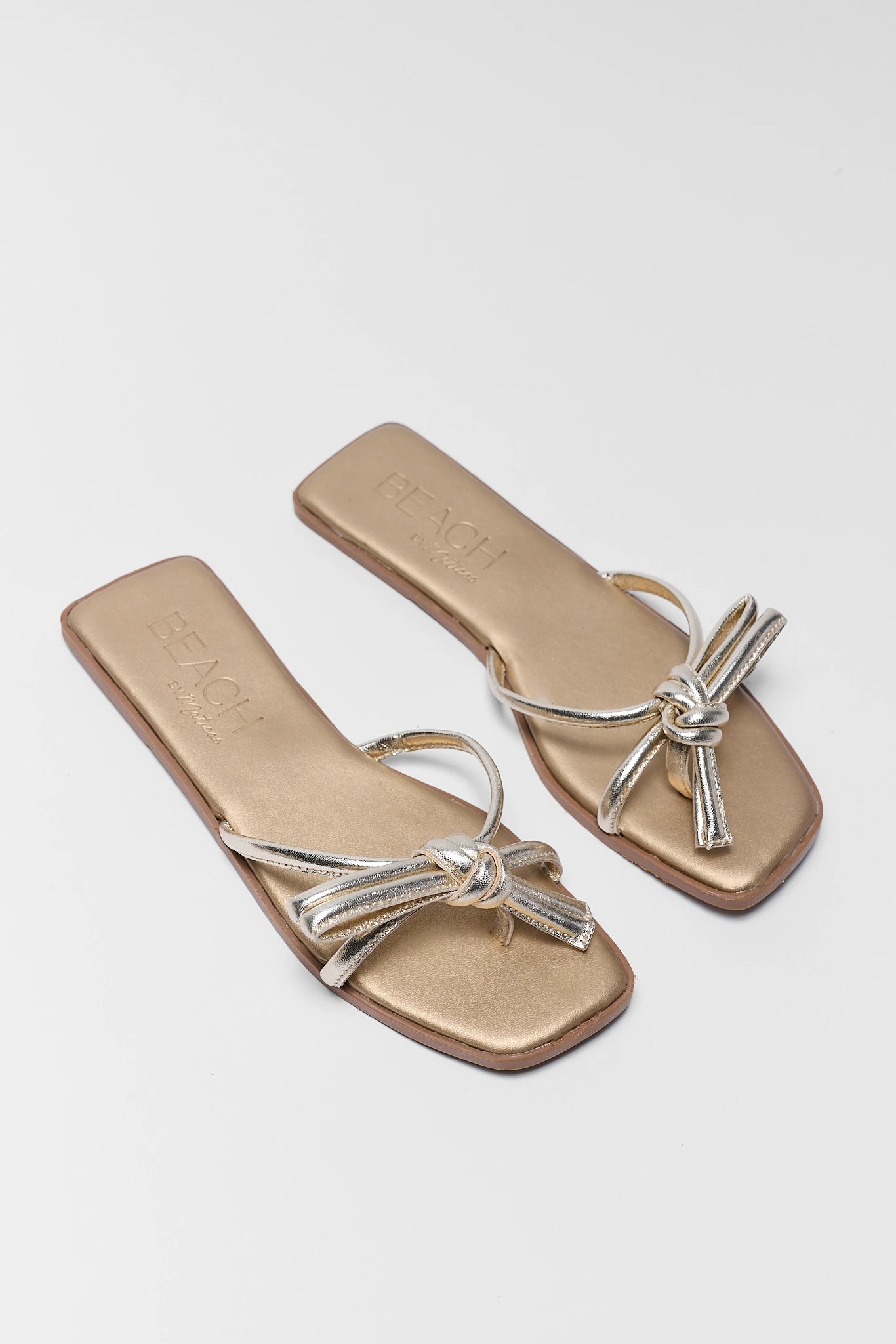Pair of gold sandals with silver straps on a white background two