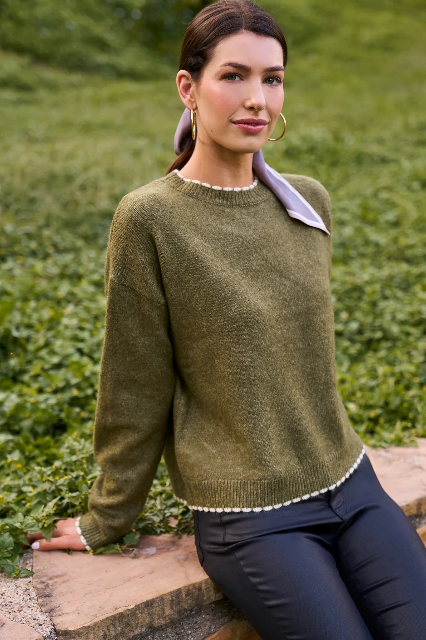 Woman wearing a olive Lottie Sweater
 with a white collar against a green outdoor background