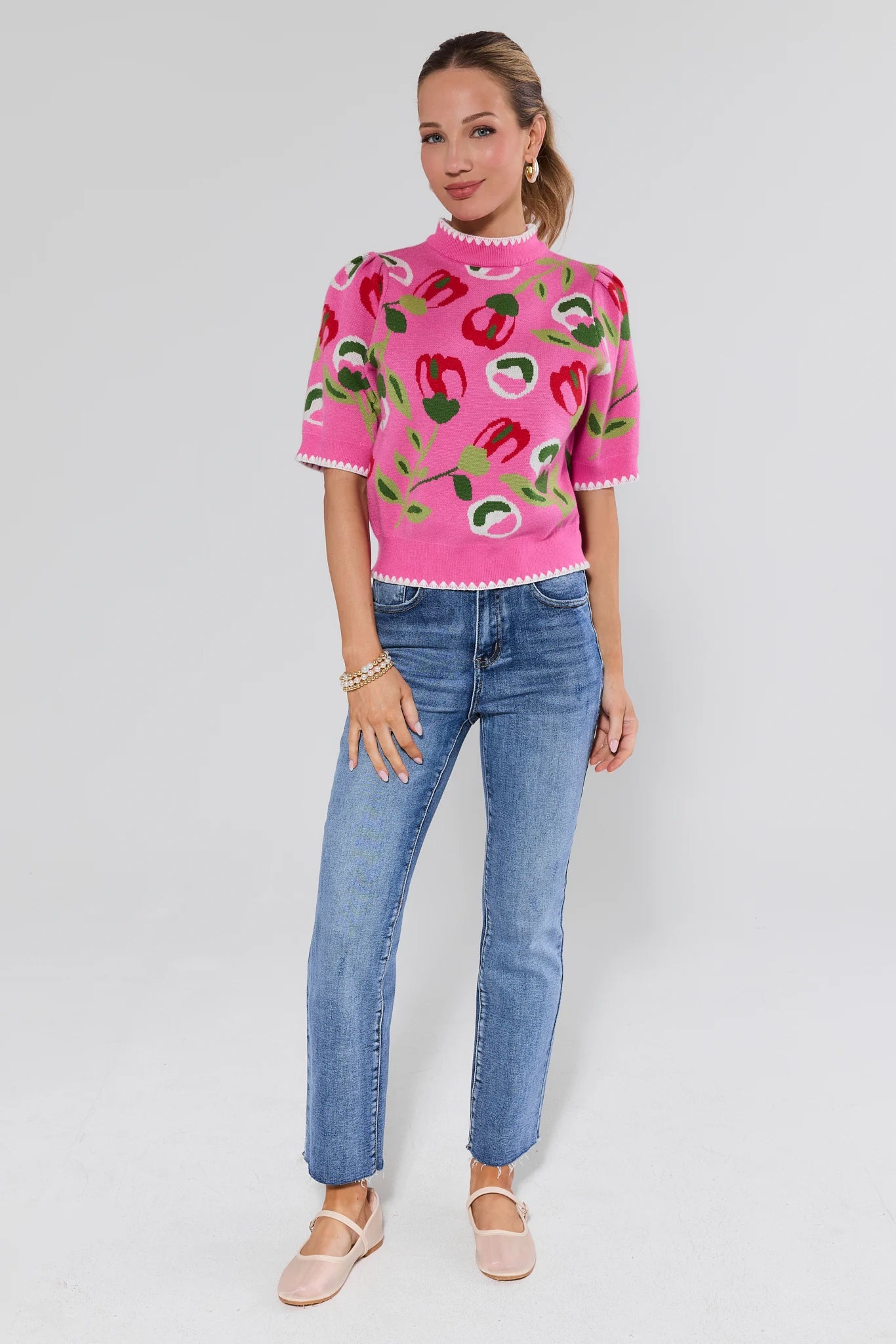 Woman wearing a pink sweater with colorful patterns and blue jeans on a white background