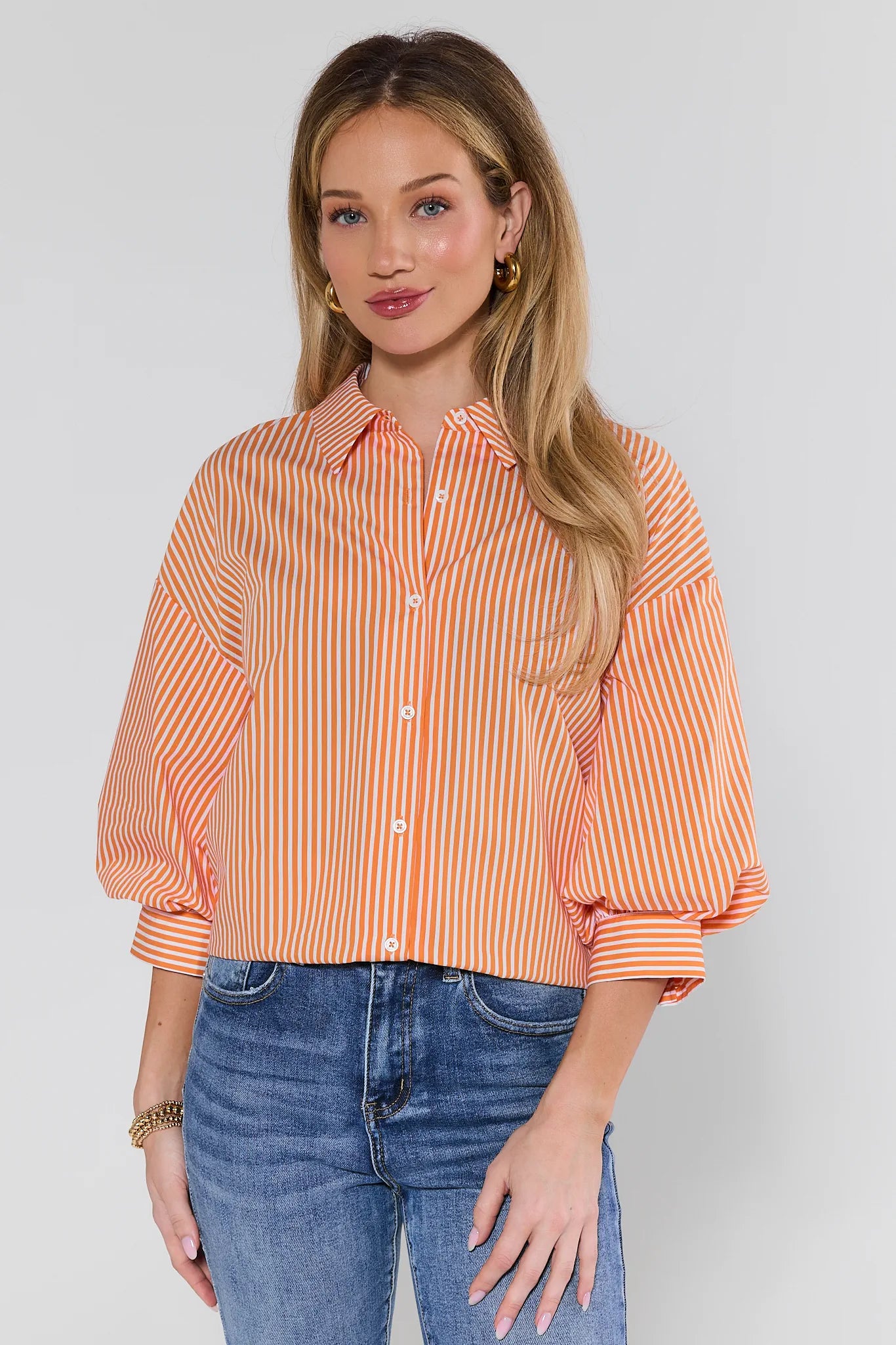 Woman wearing an orange and white striped shirt with blue jeans on a plain background