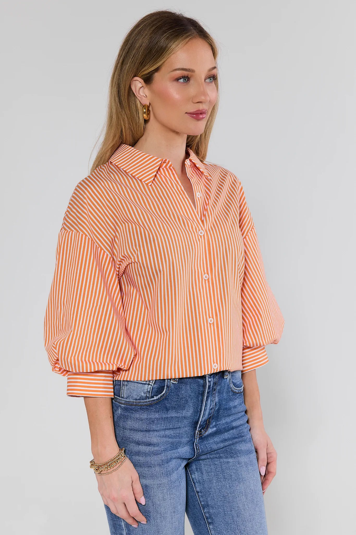 Woman wearing an orange and white striped shirt with blue jeans on a plain background