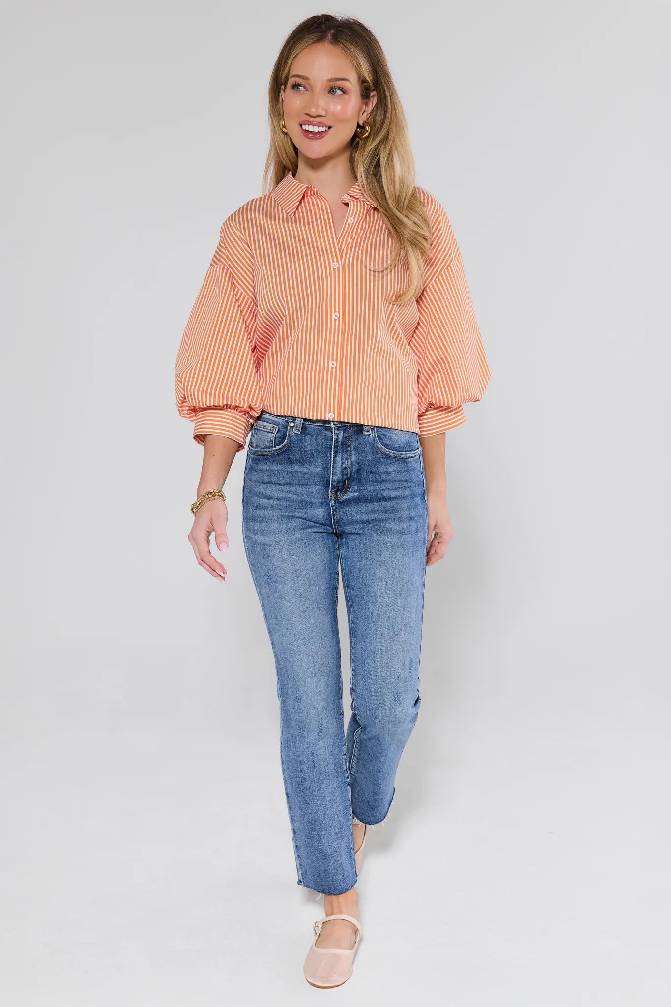 Woman wearing an orange and pink striped shirt and blue jeans on a white background