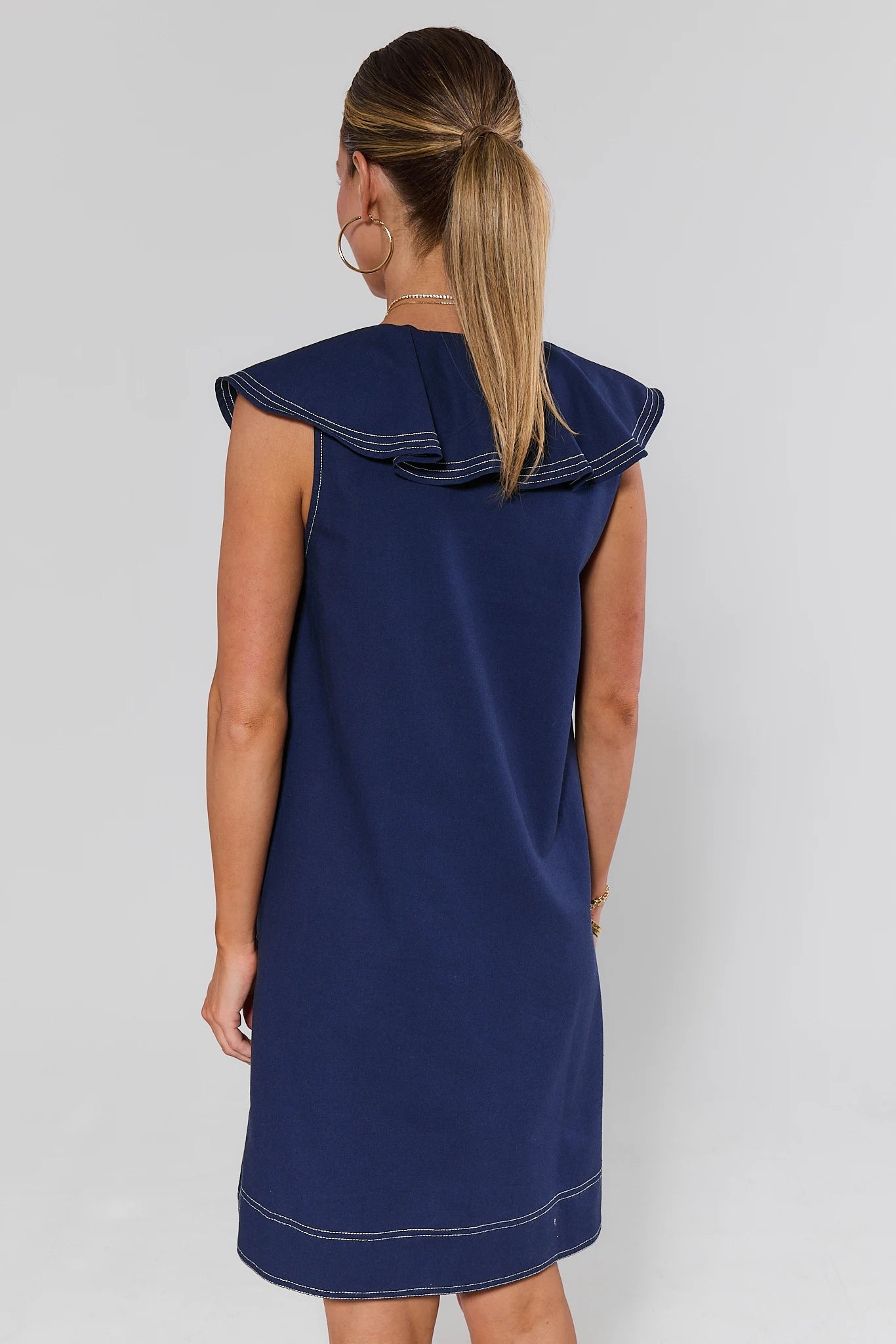 Woman standing wearing a navy blue dress with a white trim on a gray background