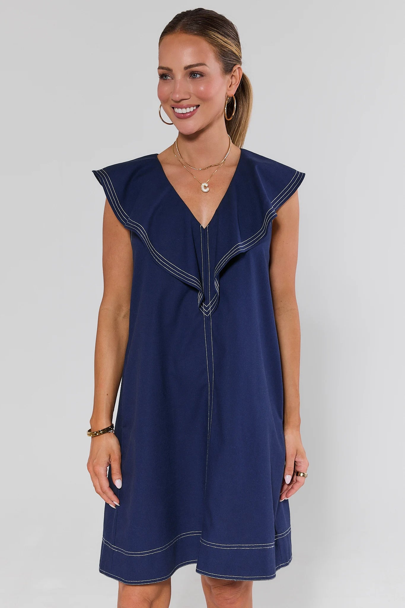 Woman wearing a navy blue dress with white trim on a plain background