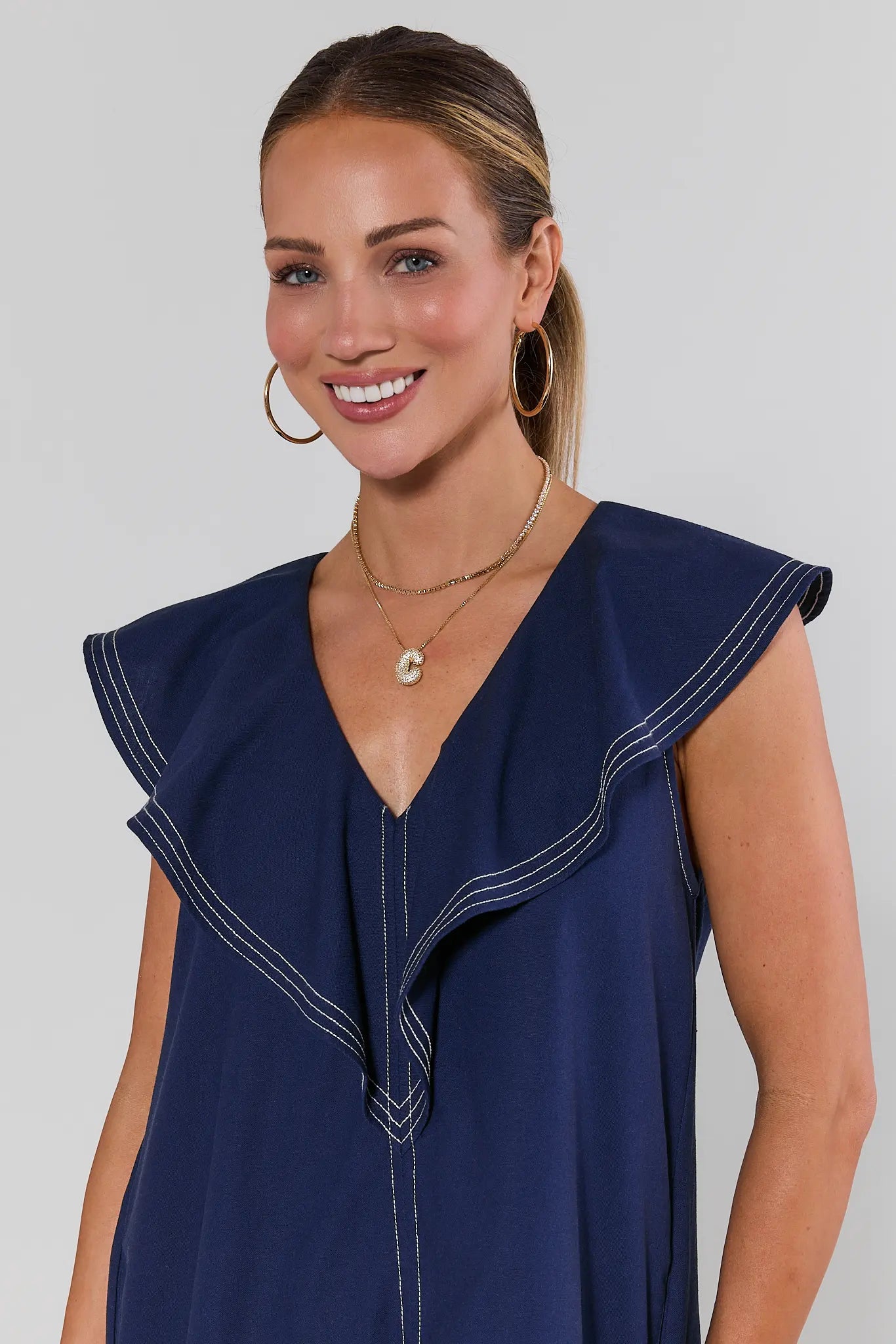 close up Woman wearing a navy blue dress with ruffled shoulders against a plain background