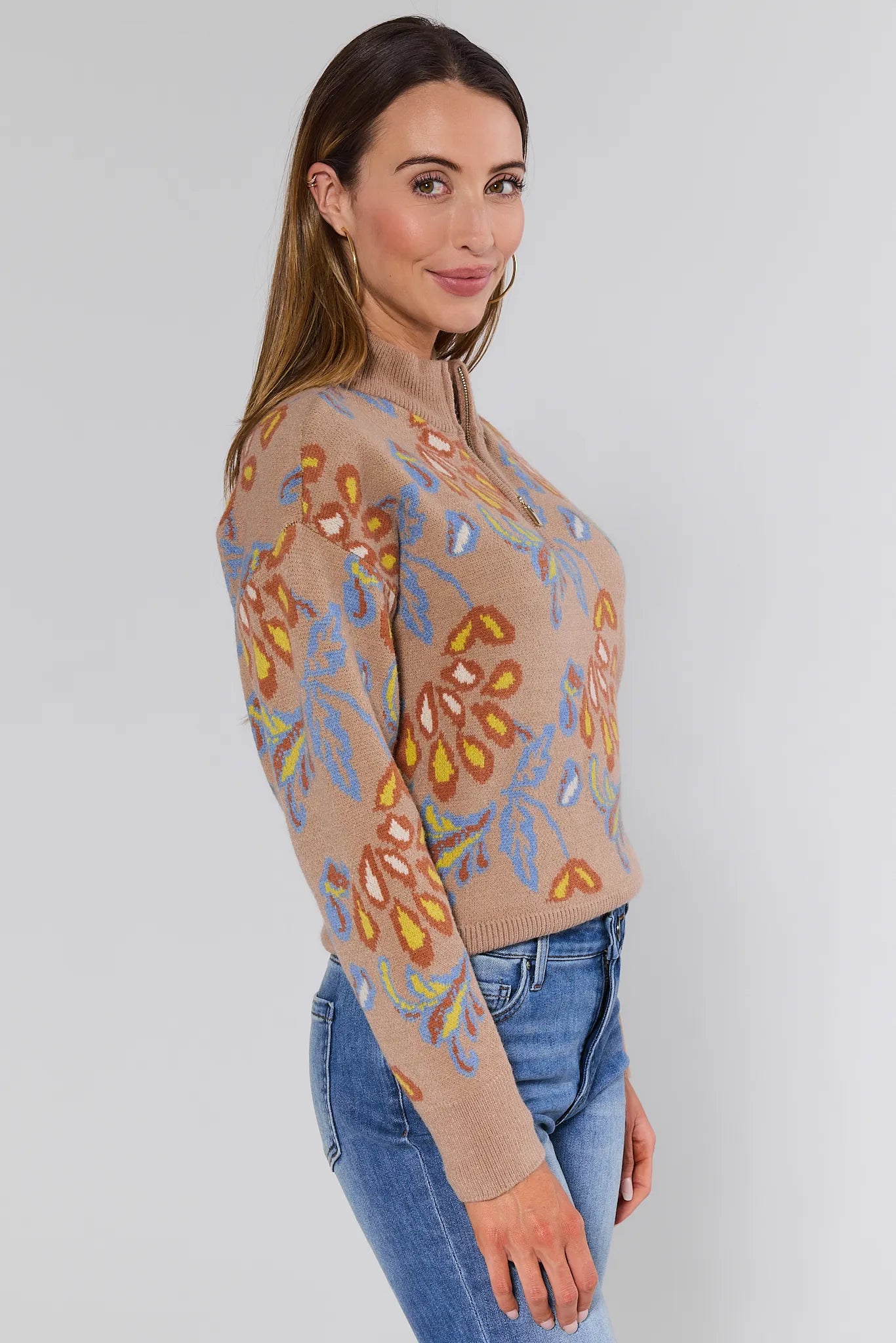 Woman wearing a floral patterned Nancy Sweater Taupe and jeans on a plain background