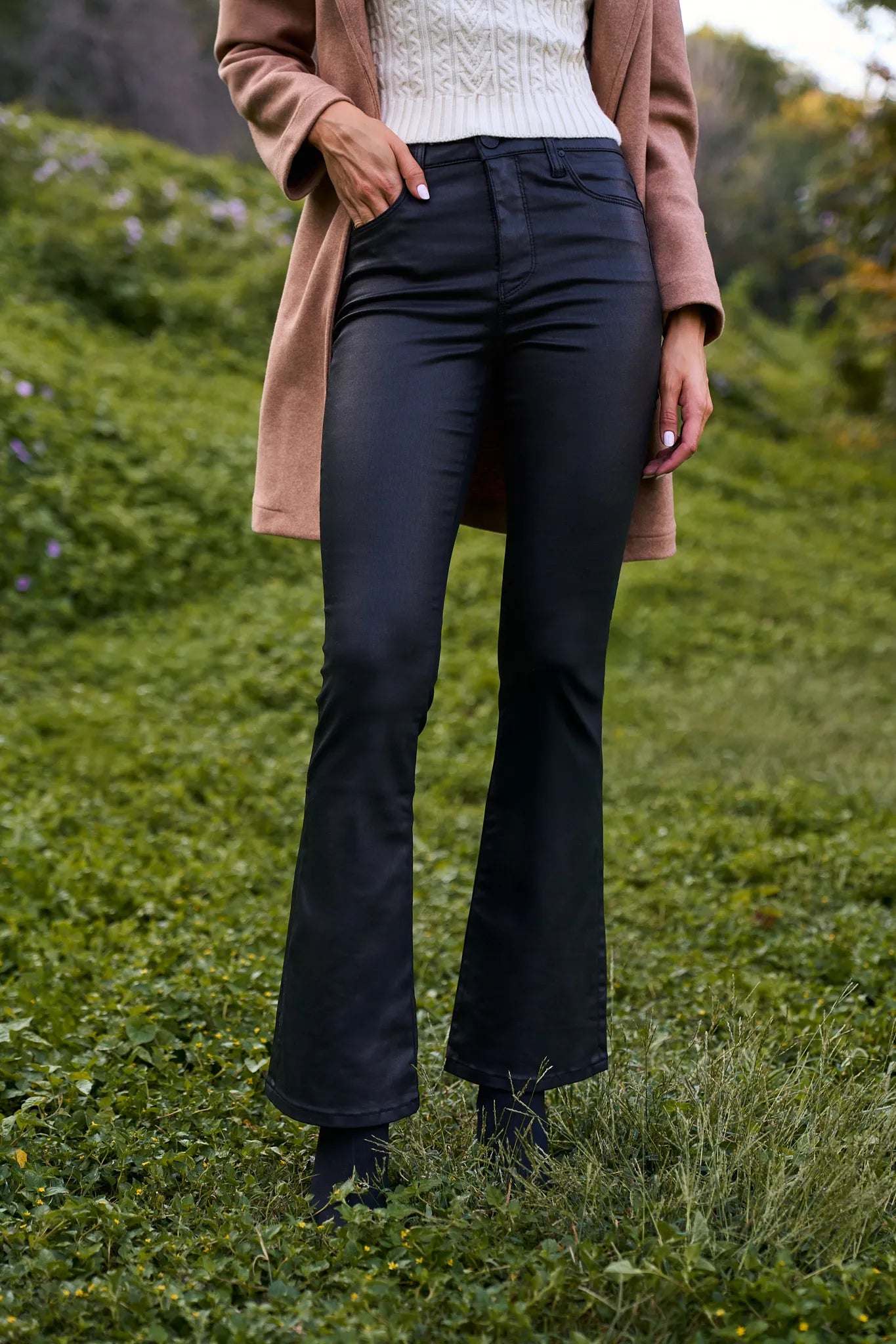 Person wearing a beige coat and Ana Wax Coated Jeans standing in a grassy area.