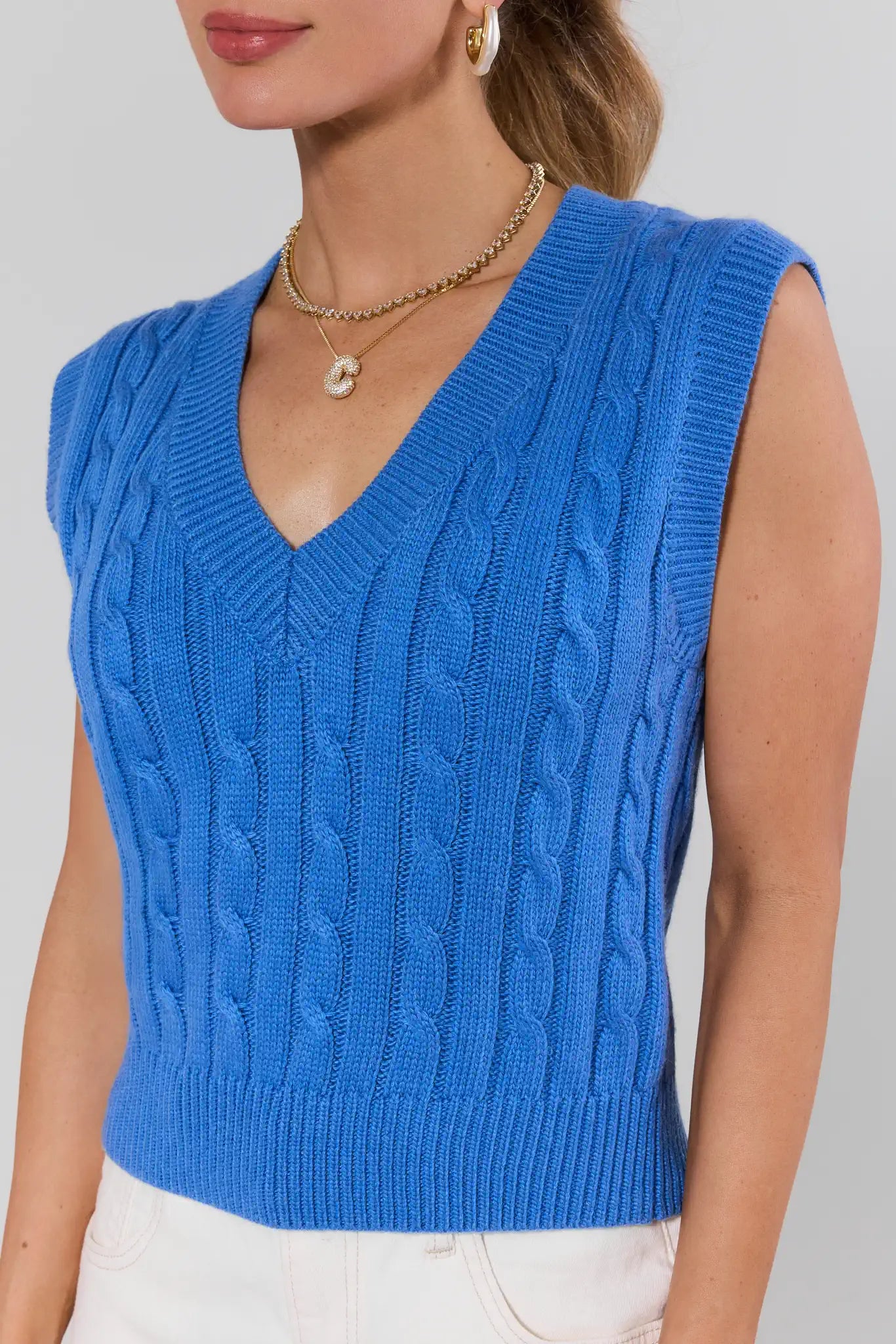 Blue knitted vest worn by a person on a plain background