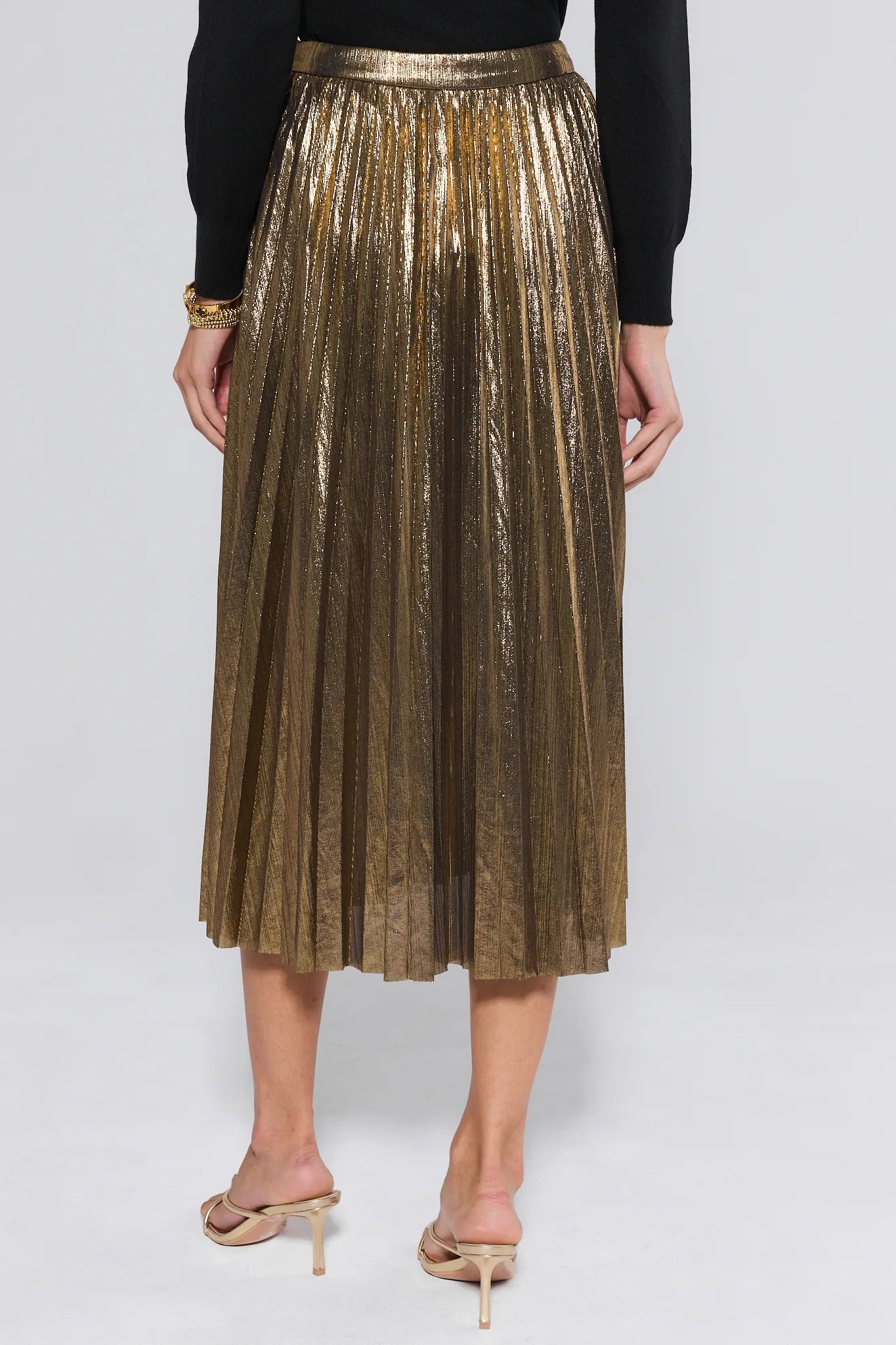 Gold pleated skirt worn by a person on a white background