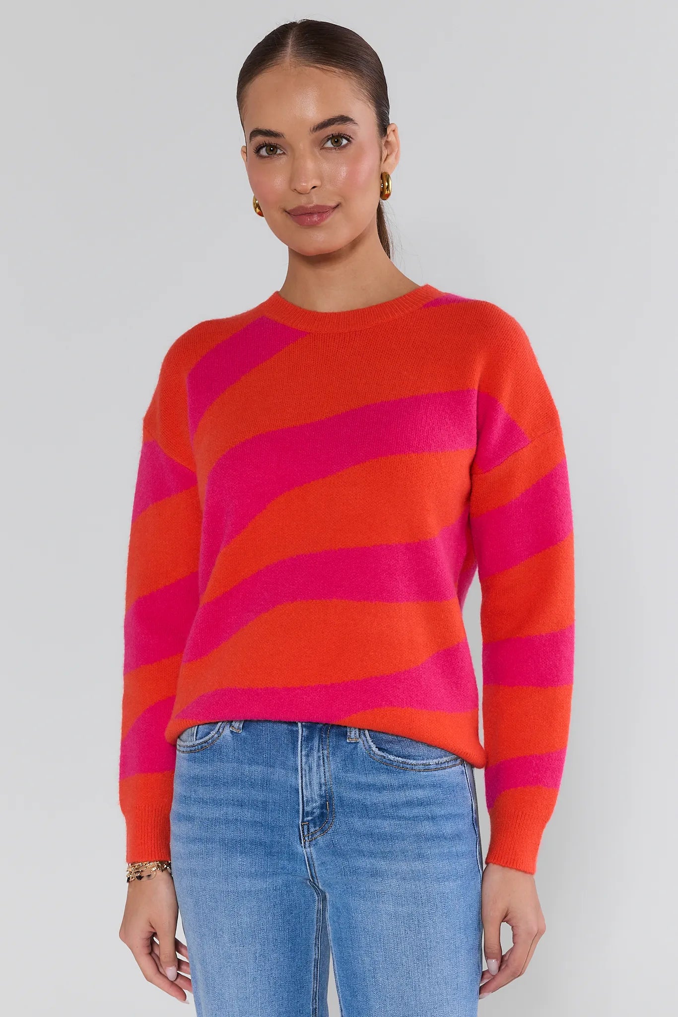 Woman wearing a red and pink striped sweater with blue jeans on a white background