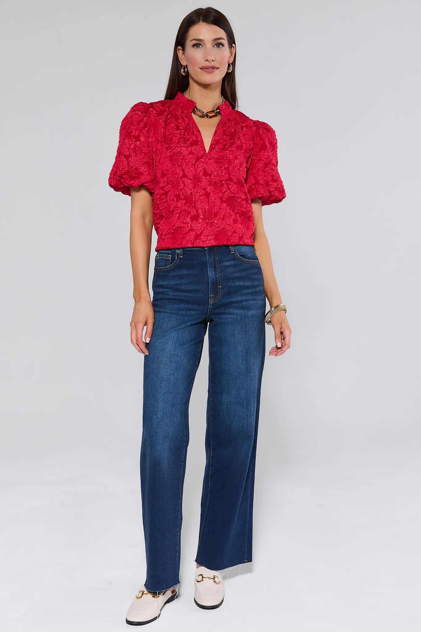 Woman wearing a red textured Teresa Floral Top with blue jeans on a white background
