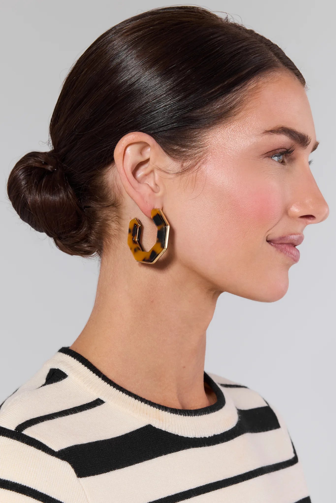 Woman wearing tortoiseshell hoop earrings with a neutral background