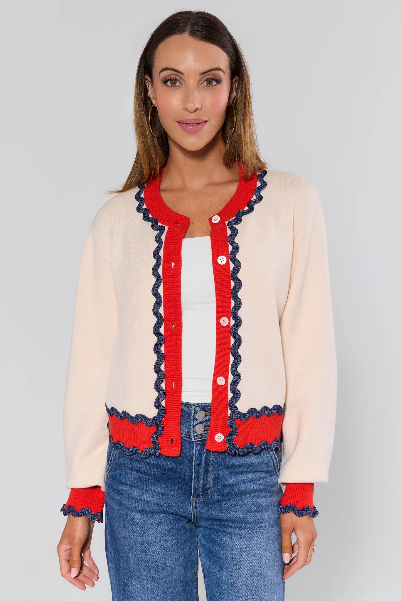 Woman wearing a cream cardigan with red and navy trim against a plain background